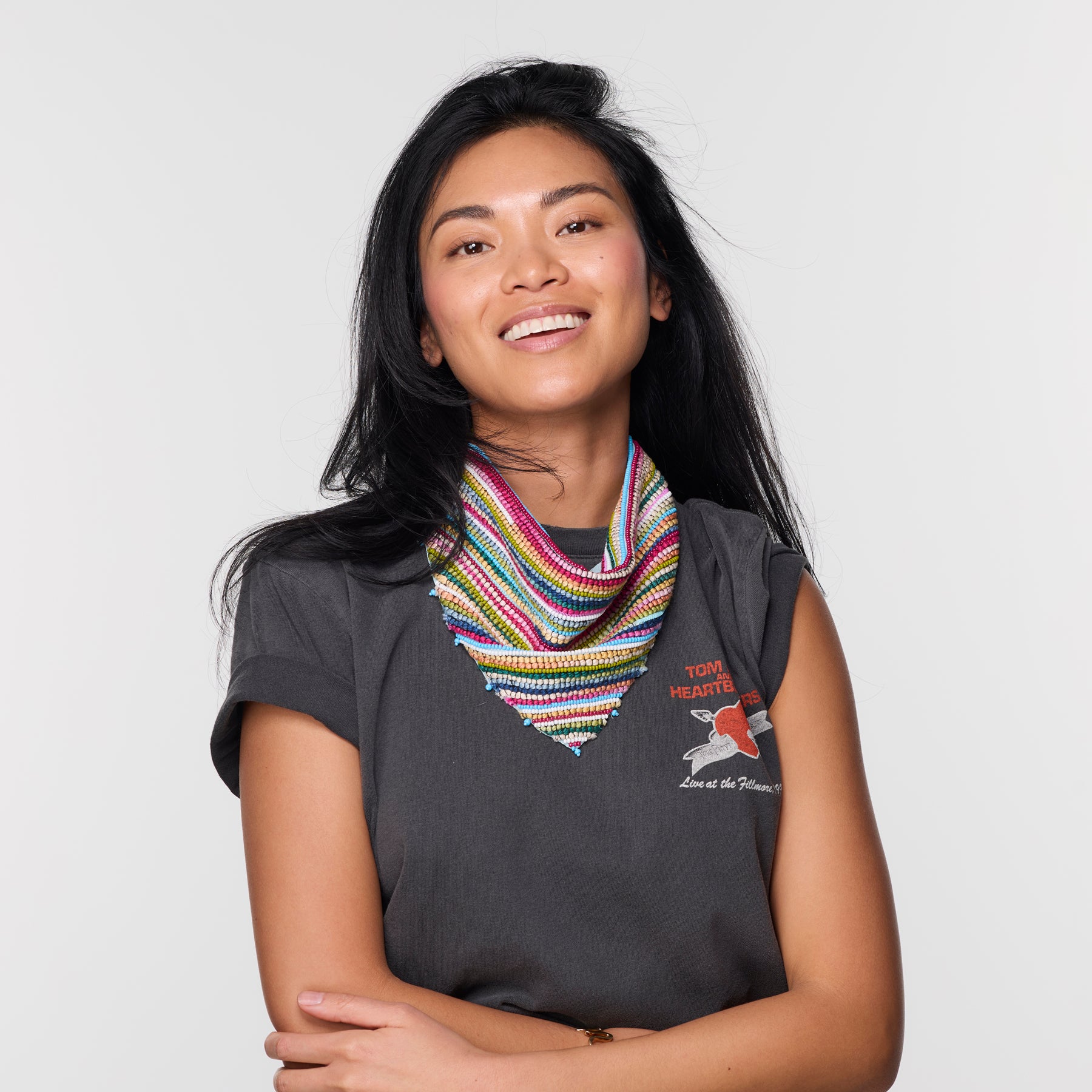 Woman wearing a dark gray t-shirt with a colorful scarf and patterned pants on a light background