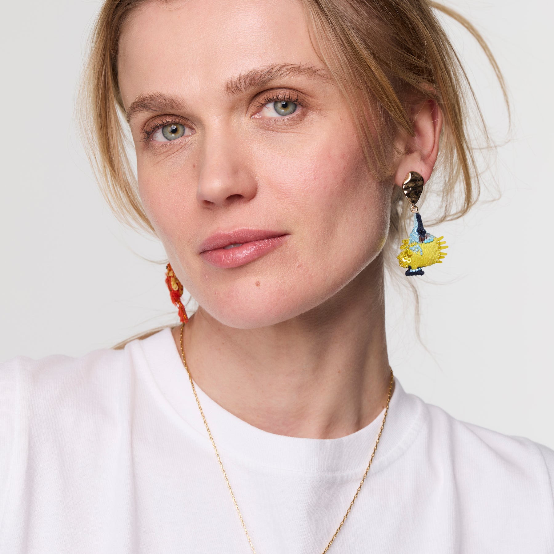 Close-up of a person wearing colorful earrings against a neutral background