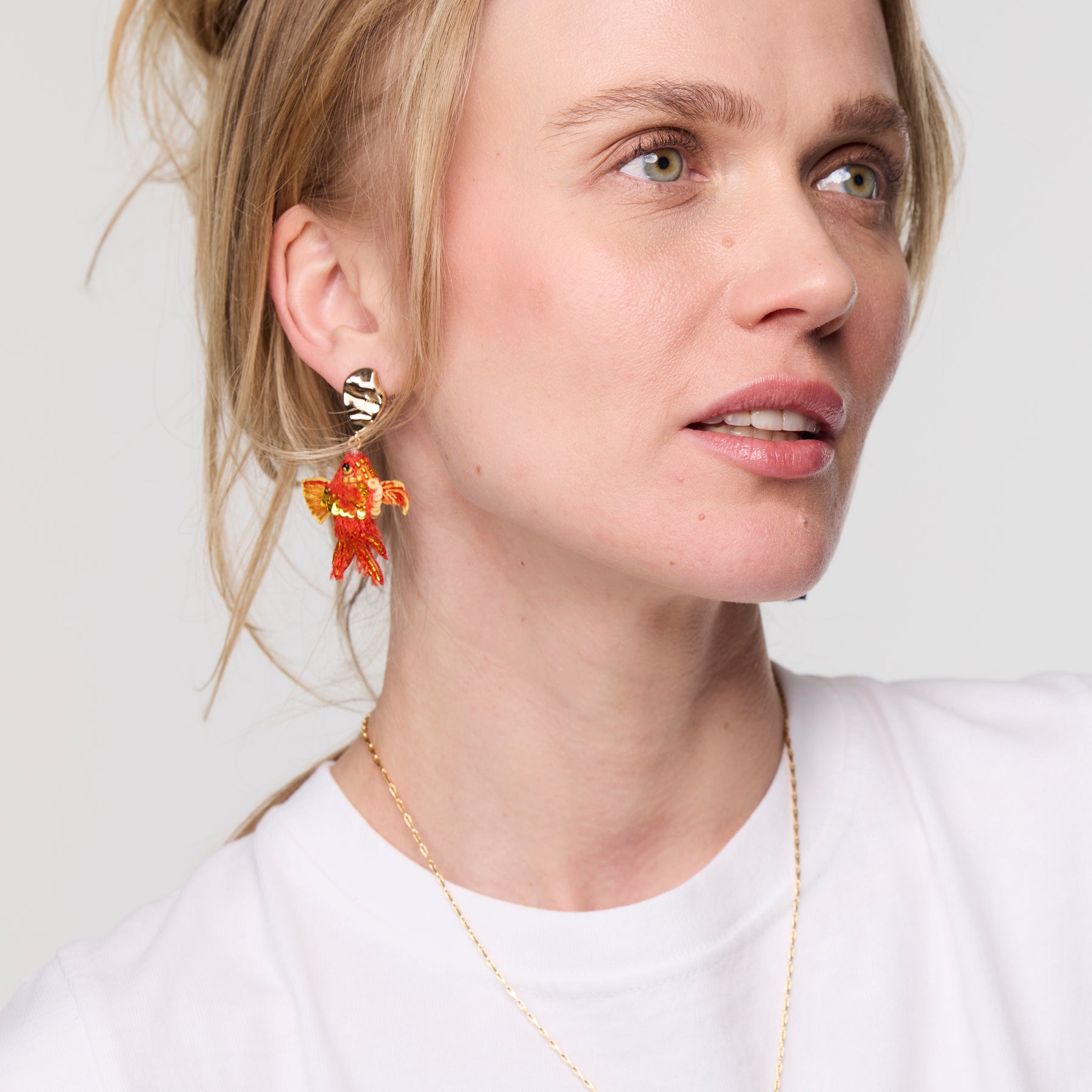 Woman wearing colorful earrings and a white shirt on a light background