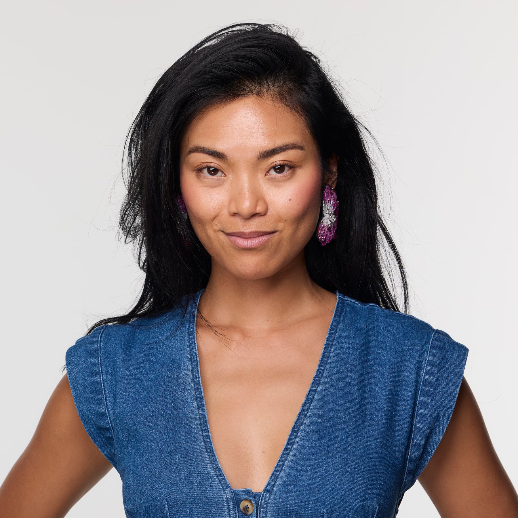 Woman wearing a blue denim top against a plain background with floral purple earring