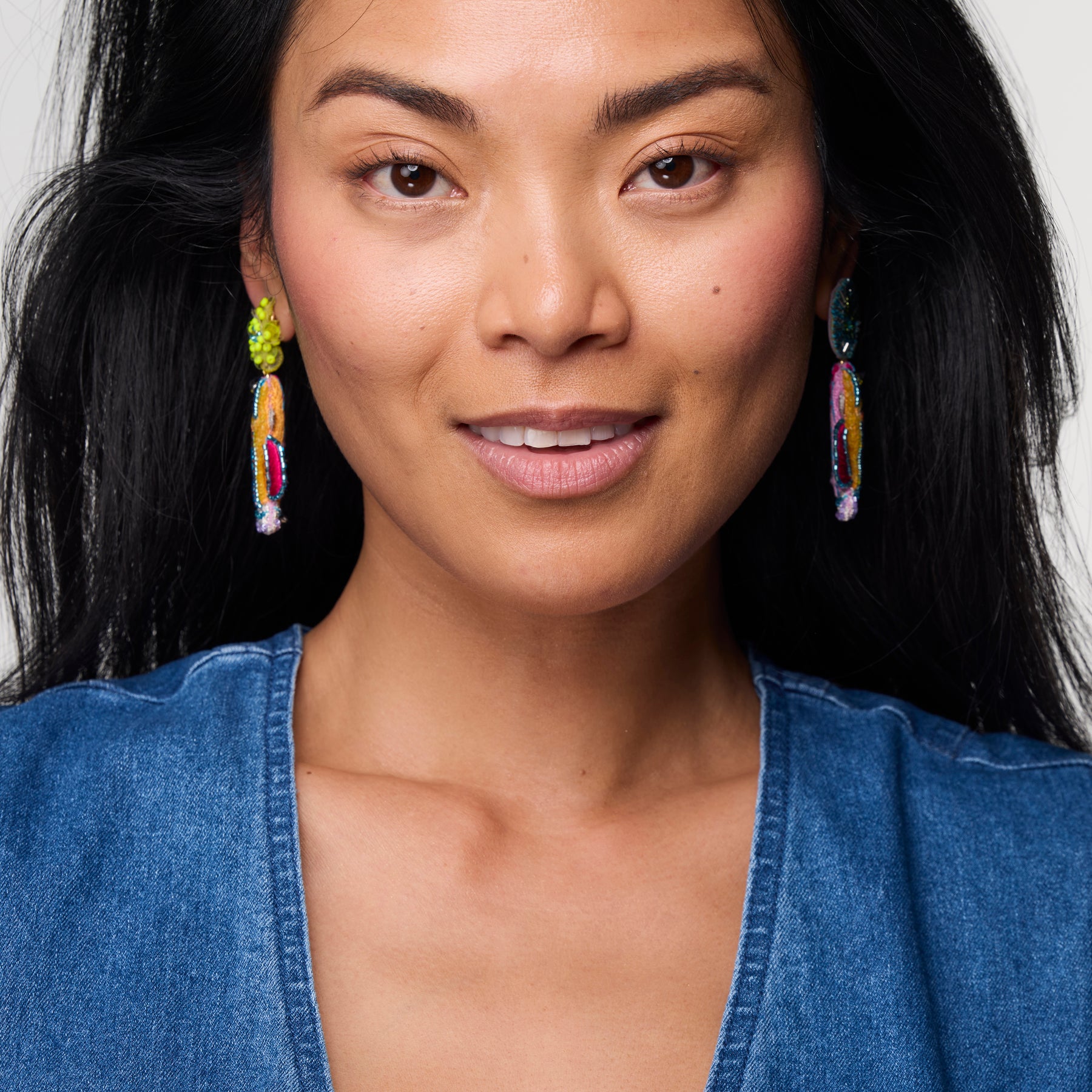 Woman wearing colorful earrings with a neutral background