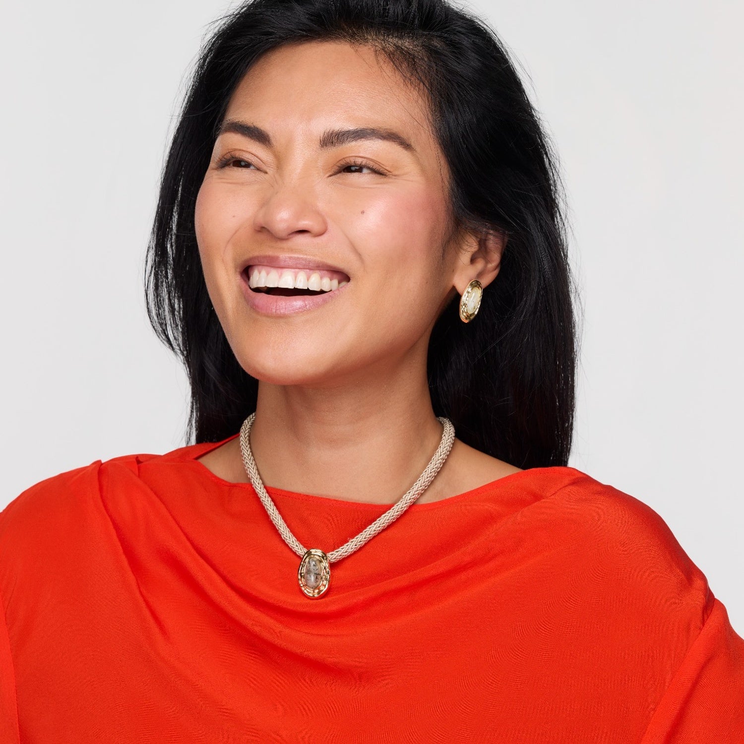 Woman wearing a red top and gold necklace with a white background