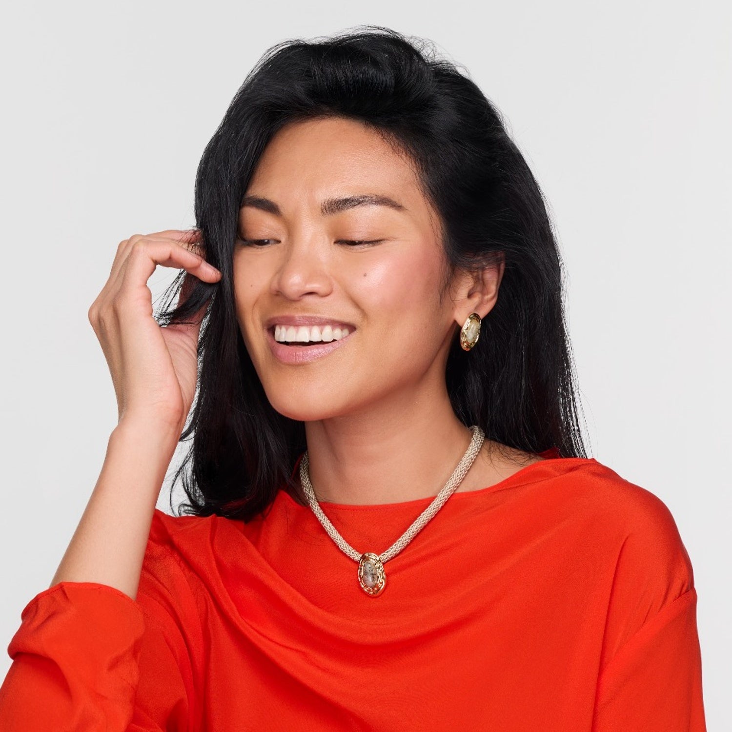 Woman wearing a red top and gold necklace against a plain background