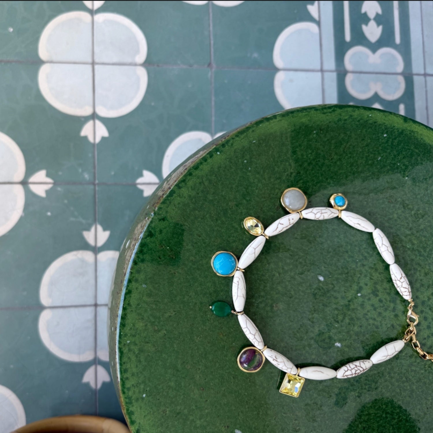 Bracelet with gemstones on a green cushion against a patterned tile background