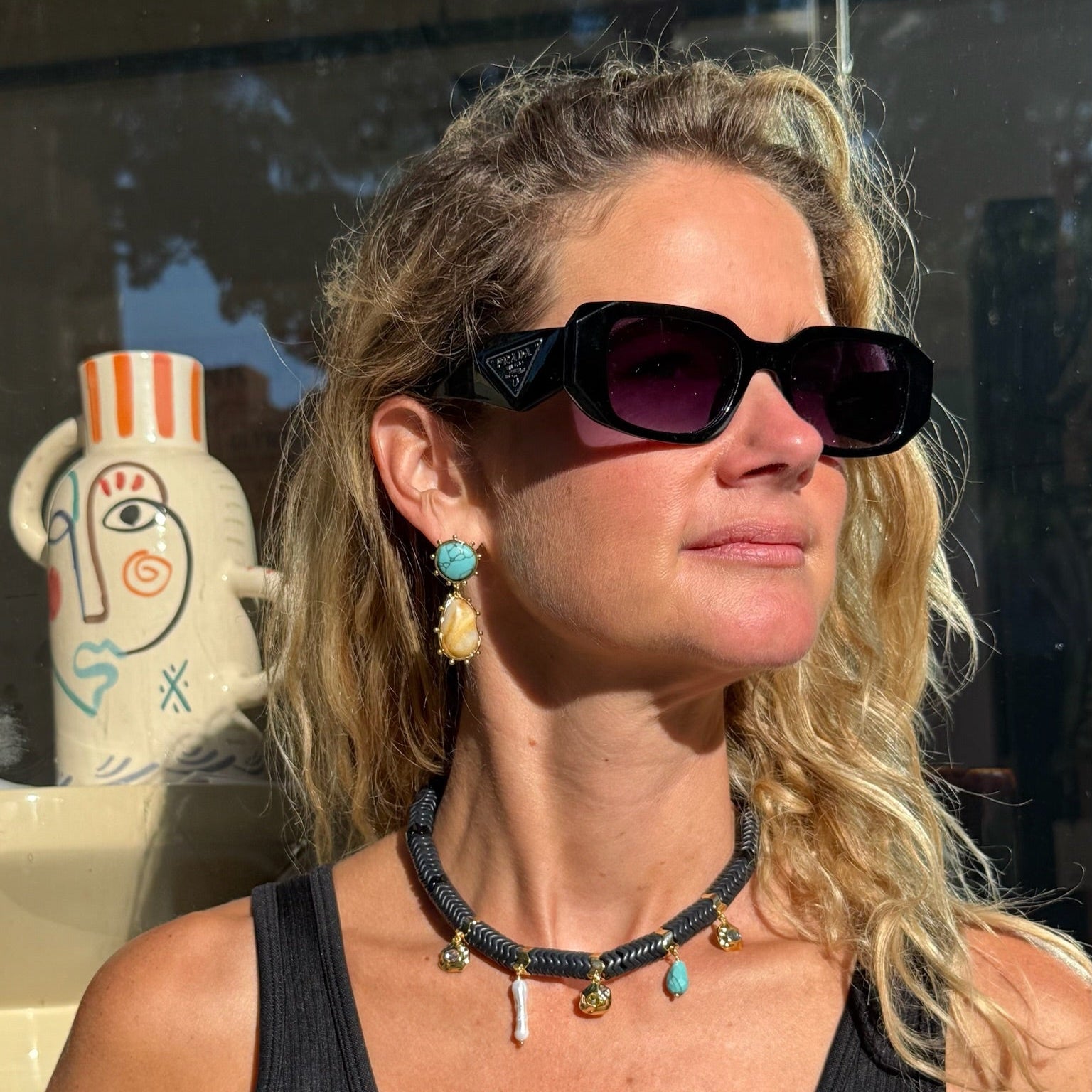 Maggie wearing sunglasses, double drop earrings, and black charm necklace