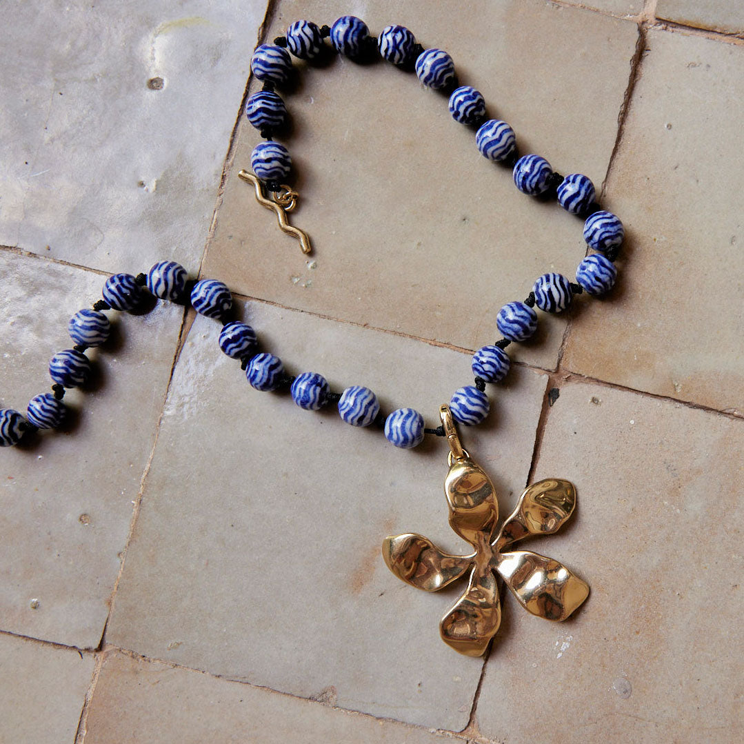 Blue and White Marbled Glass Bead Strand with Gold Organic Flower Pendant Charm Staged on Tiles