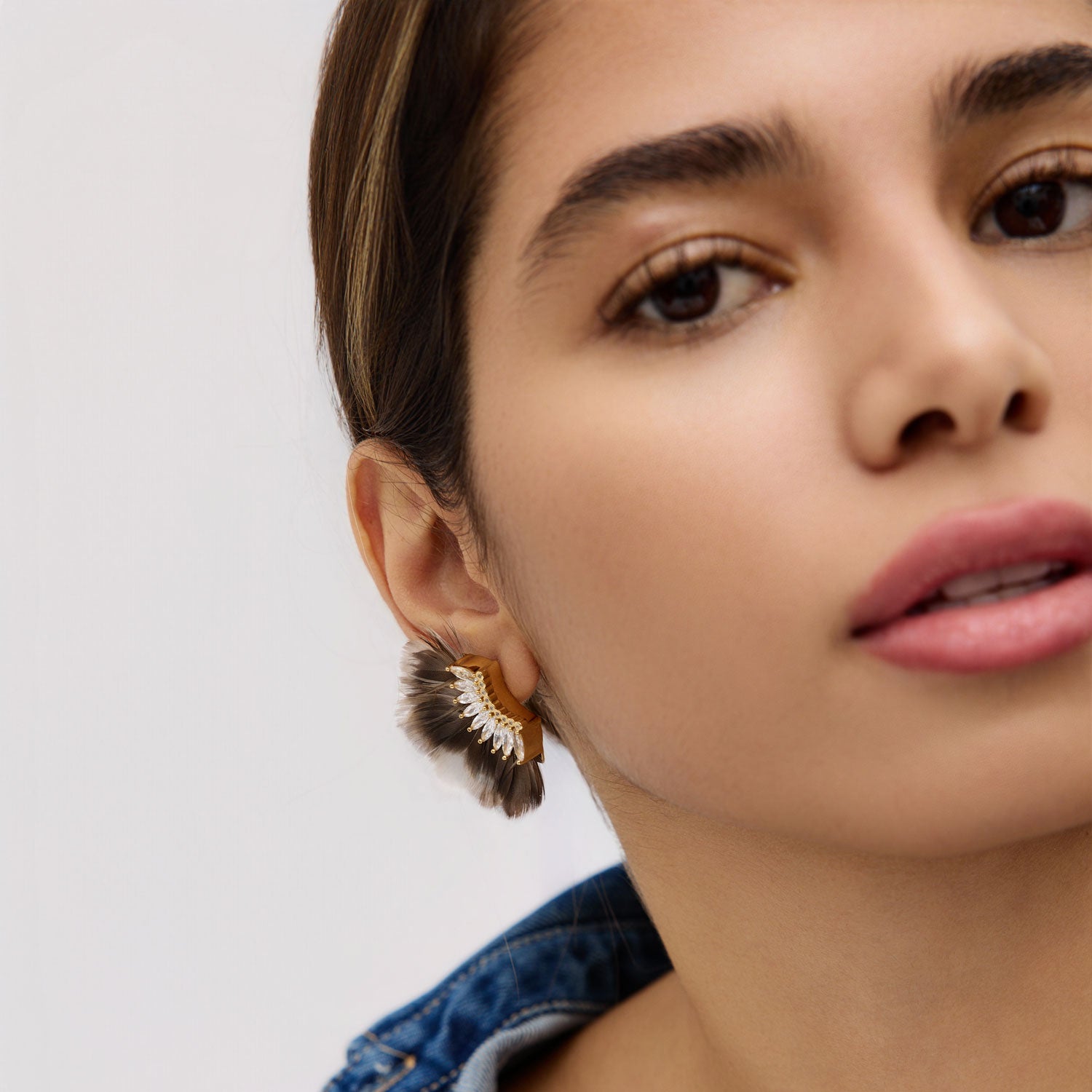 Close-up of a woman wearing a feathered earring against a plain background