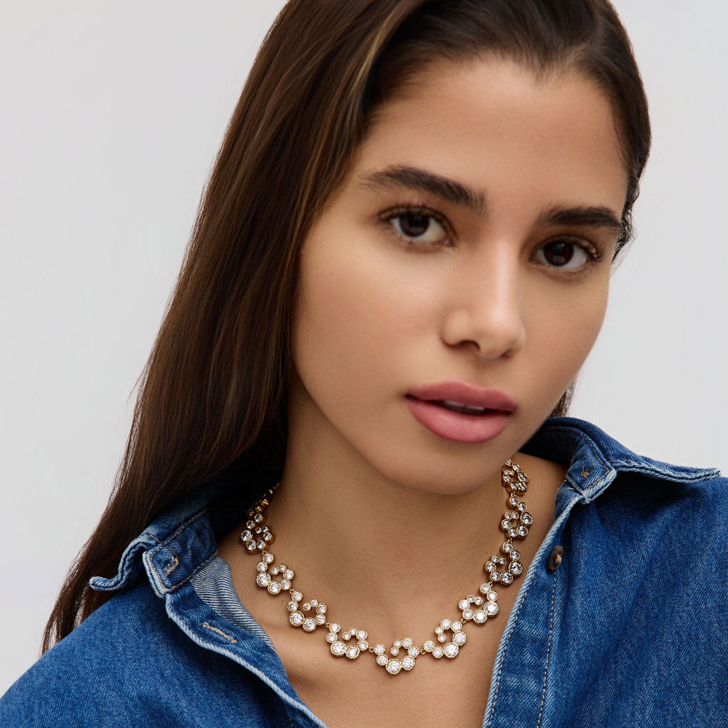 Woman wearing denim top and crystal necklace with white background