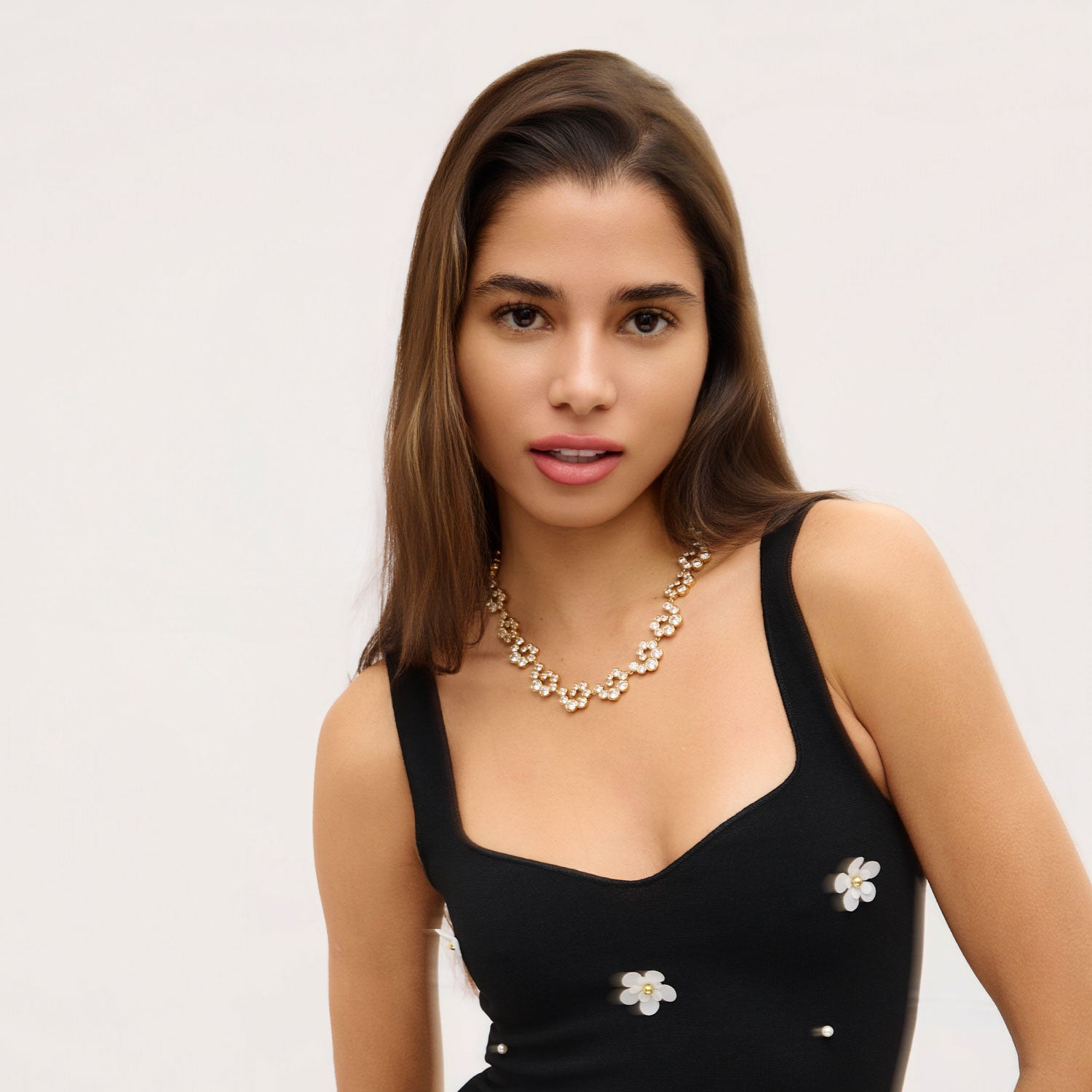 Woman wearing black top with flowers and crystal necklace with white background