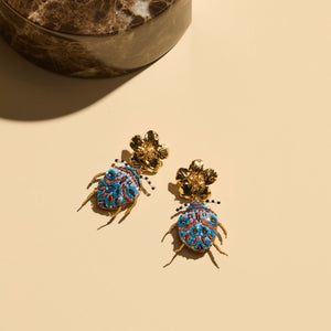 Blue Beaded Bug Drop Earrings with Gold Flower Topper Staged on Cream Background with Marble Accent