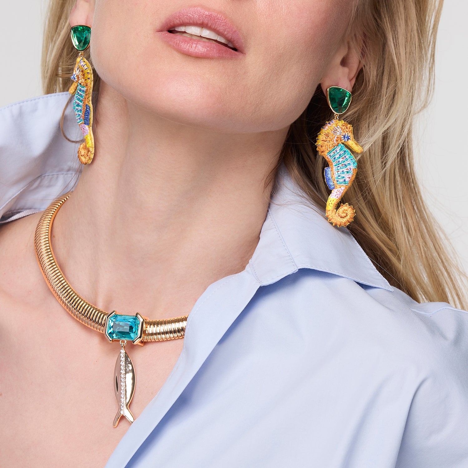 Close-up of a person wearing gold and turquoise Genesis Earrings with a plain background