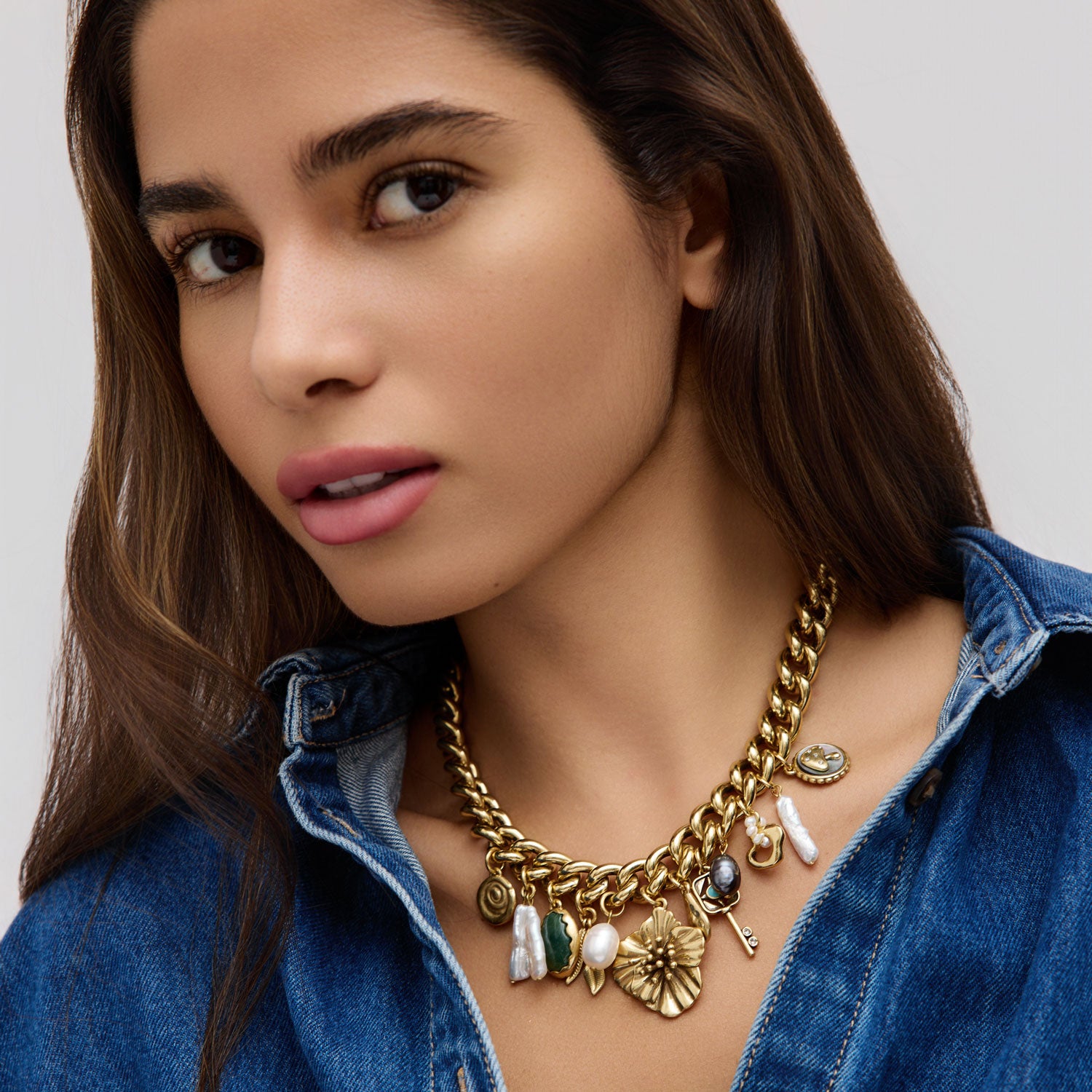 Woman wearing a gold necklace with various pendants against a neutral background