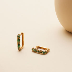 Emerald and Gold Hoop Earrings Staged on Flat Cream Surface with Vase in Background