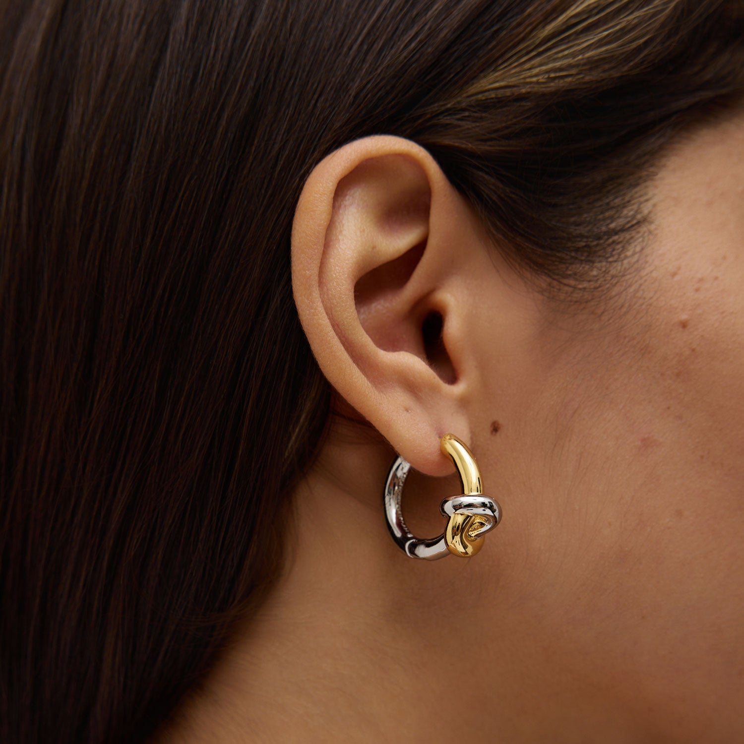 Close-up of an ear wearing a gold and silver hoop earring.