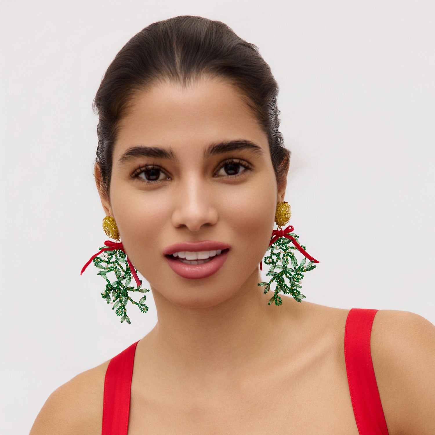 Woman wearing festive mistletoe earrings with a plain background