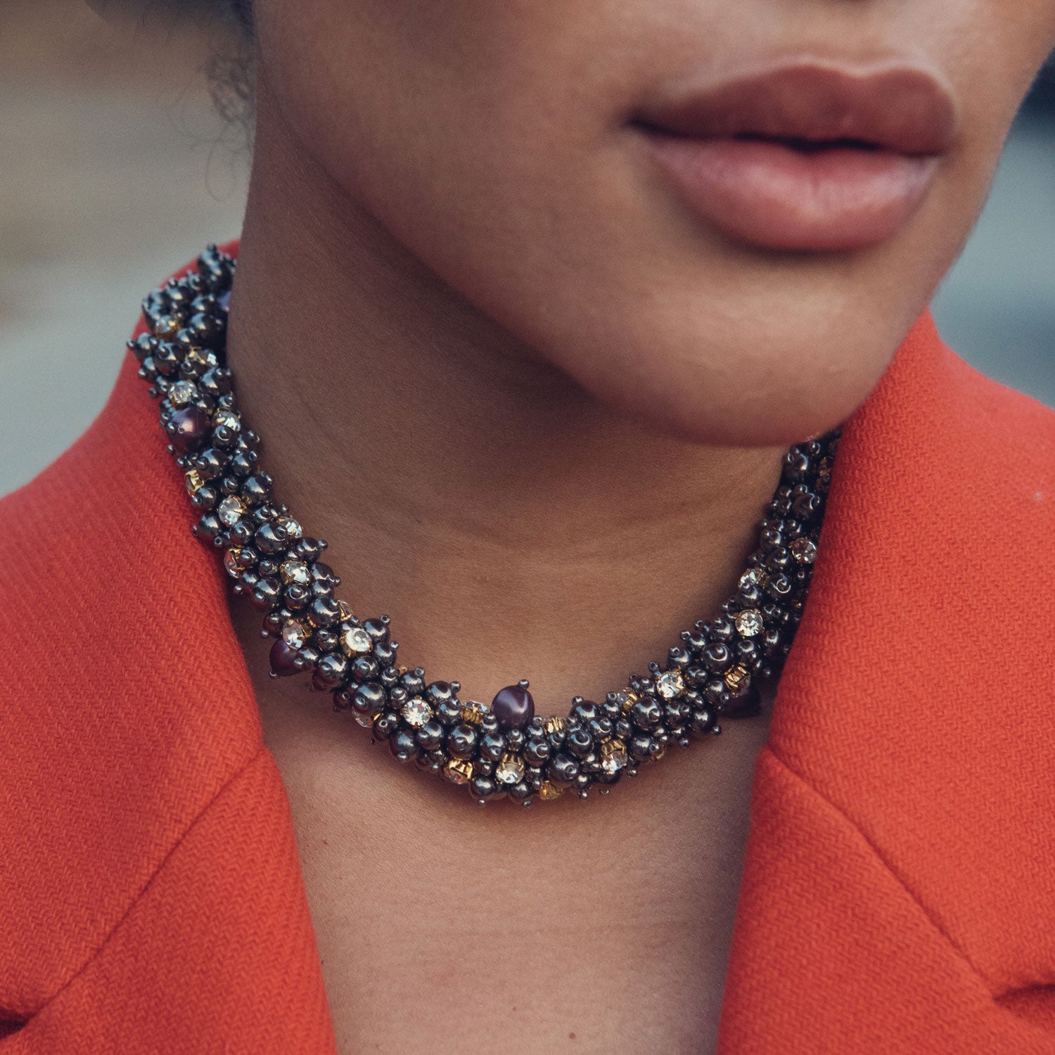 Close-up of a person wearing a sparkling necklace with an red blazer.