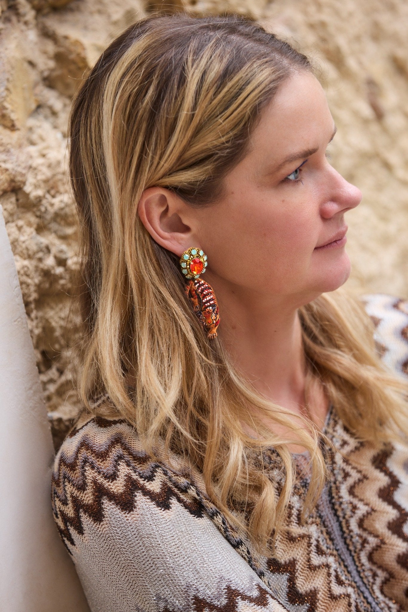 Woman wearing colorful earrings with a patterned sweater against a natural background