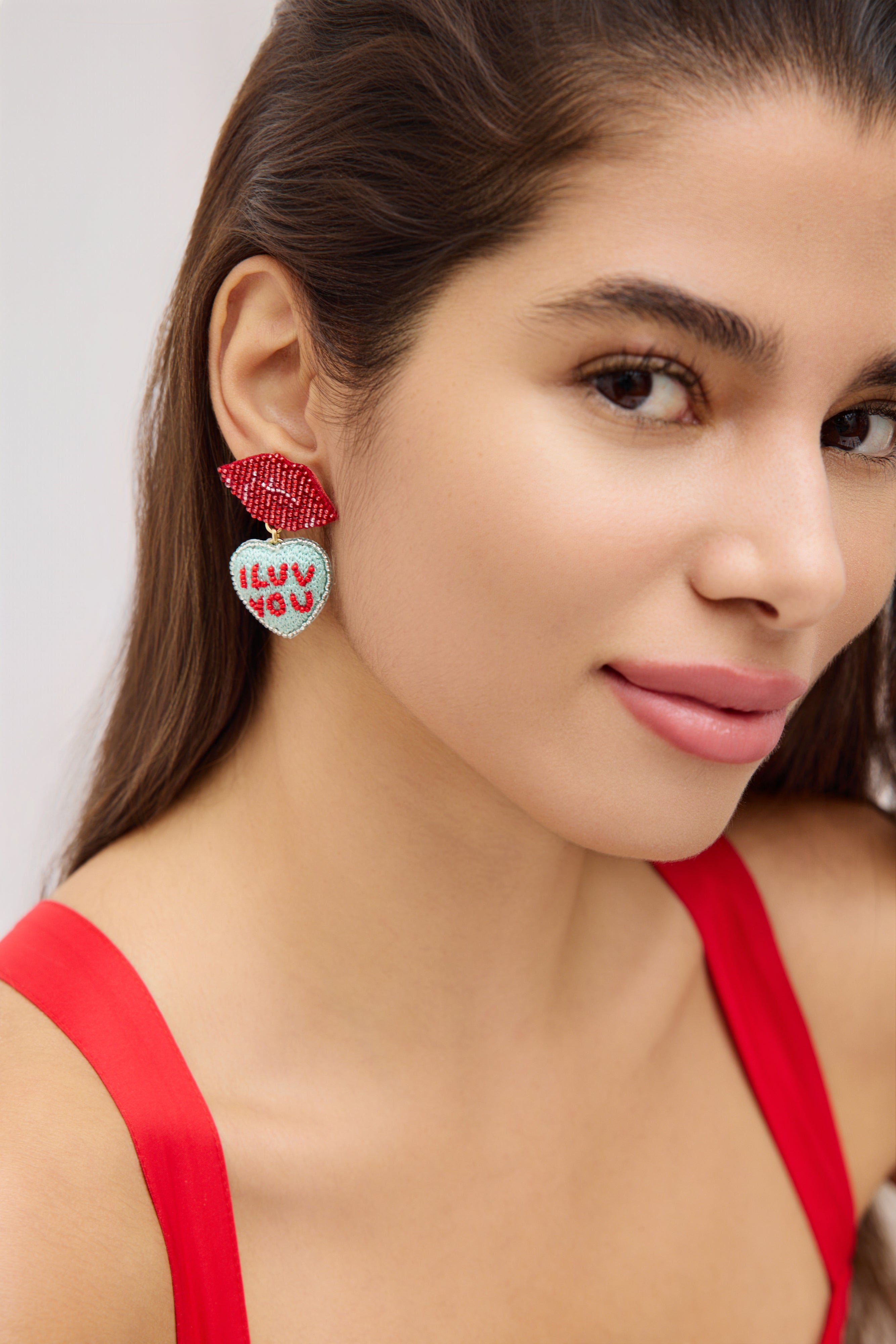 Woman wearing red earrings with heart designs on a plain background
