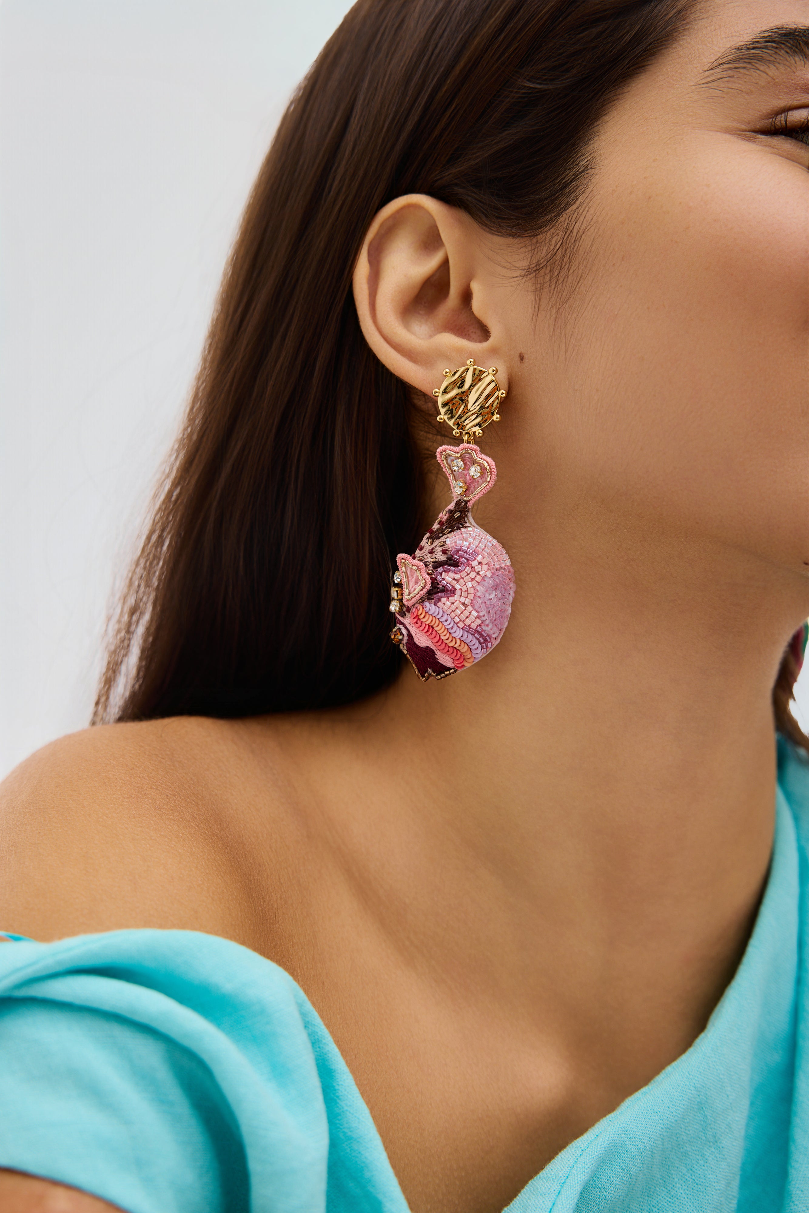 Close-up of a woman wearing a colorful fish earring with a light blue top.