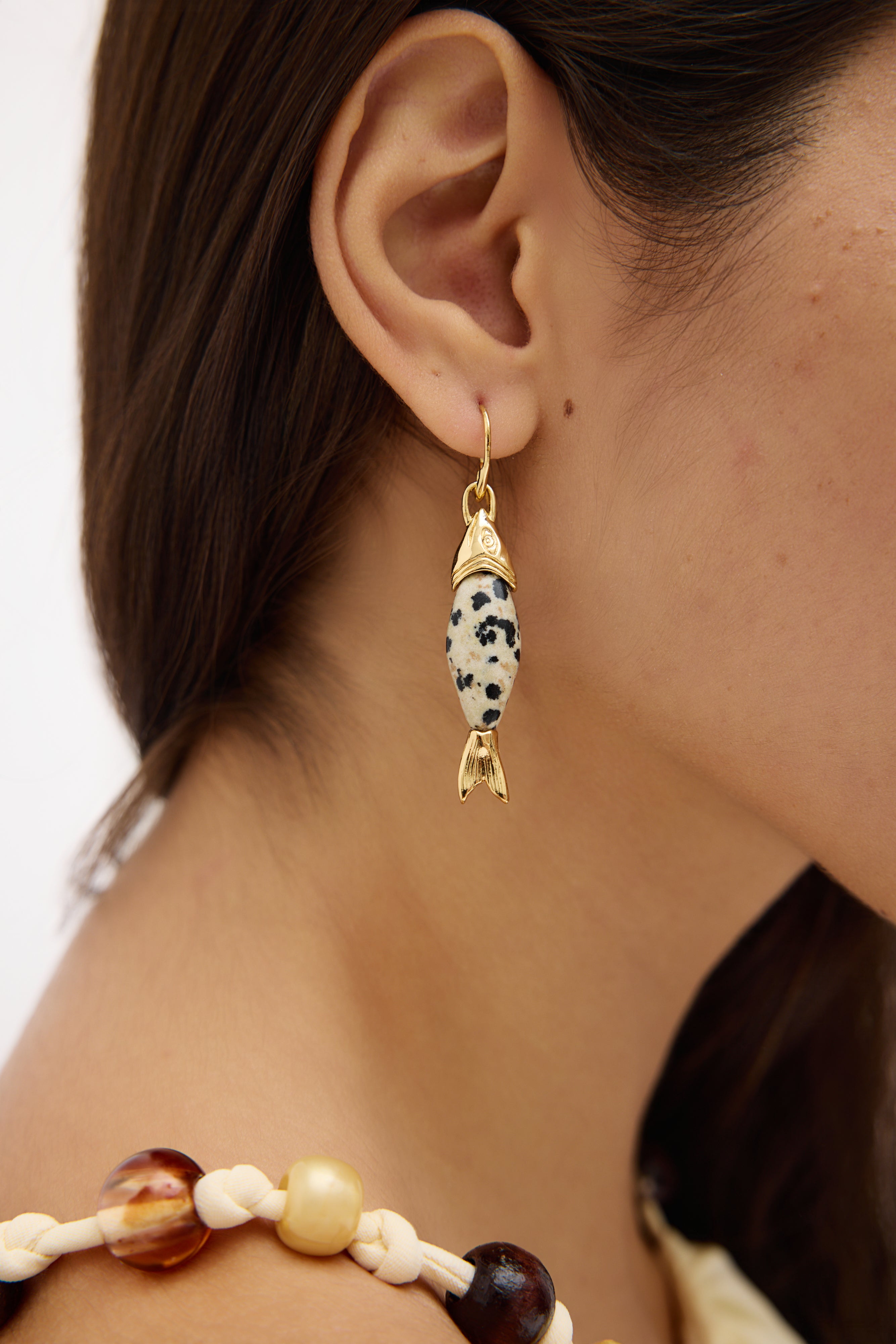 Close-up of a person wearing a gold earring with a black and white bead design.