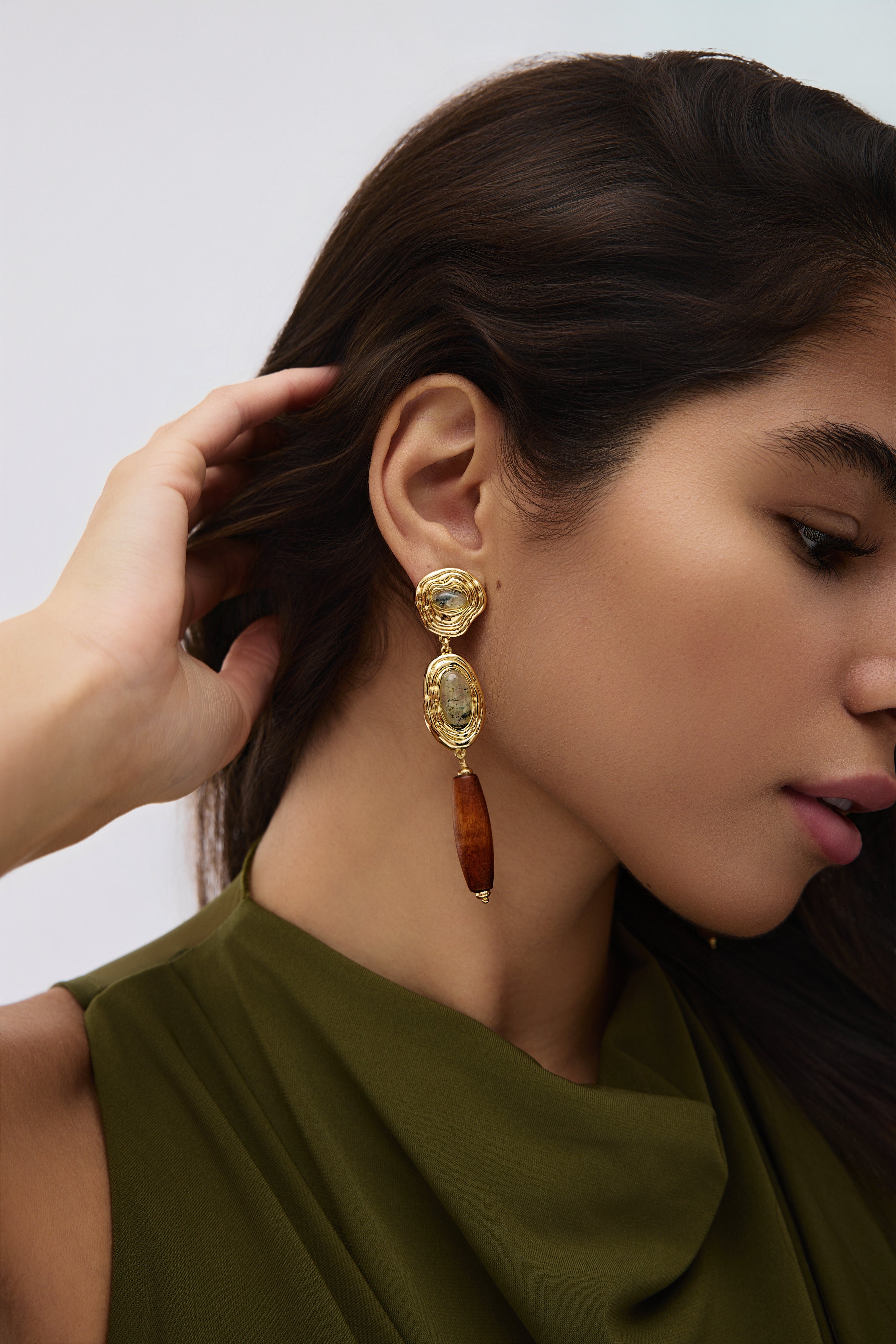 Woman wearing a gold and brown earring against a neutral background