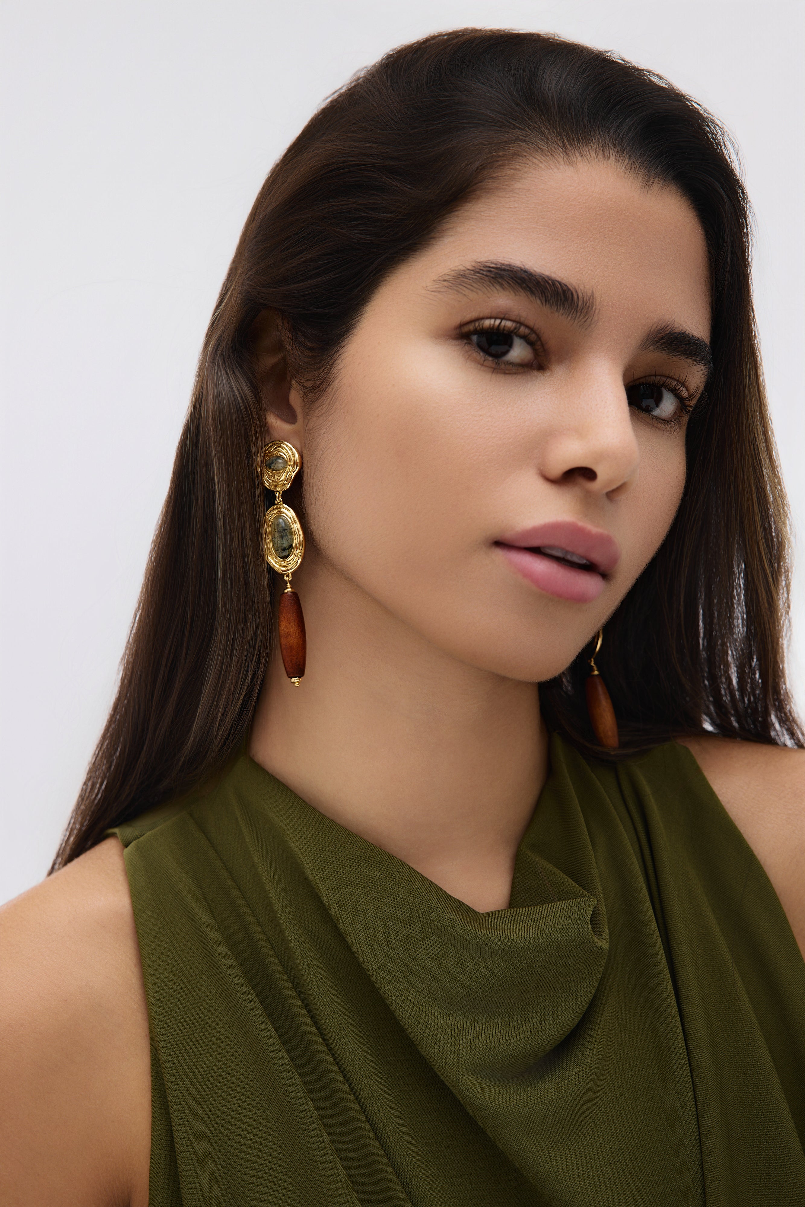 Woman wearing gold earrings with brown stones against a white background