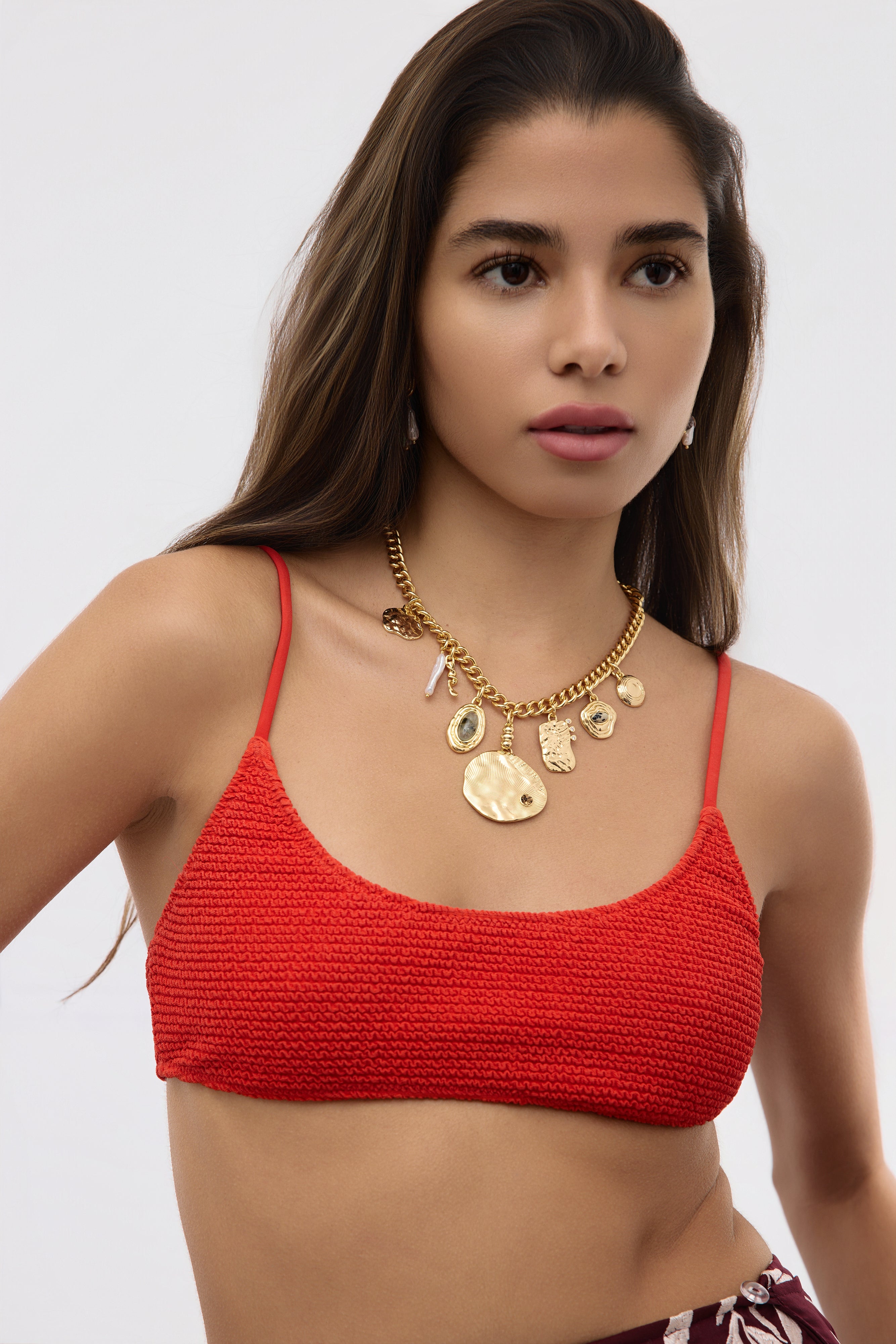 Woman wearing a red crochet top and gold jewelry on a white background