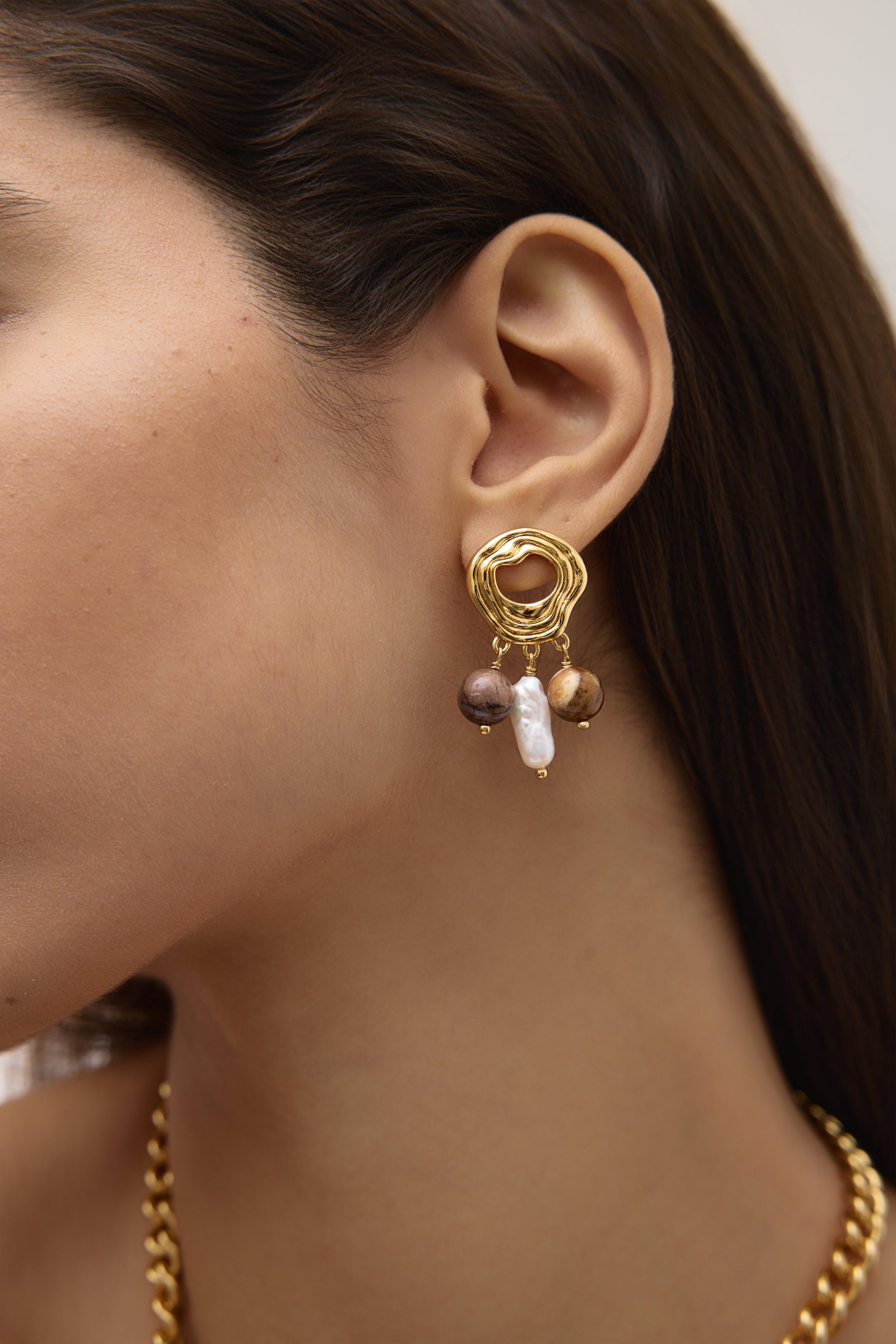 Close-up of a gold earring with pearls worn by a person.