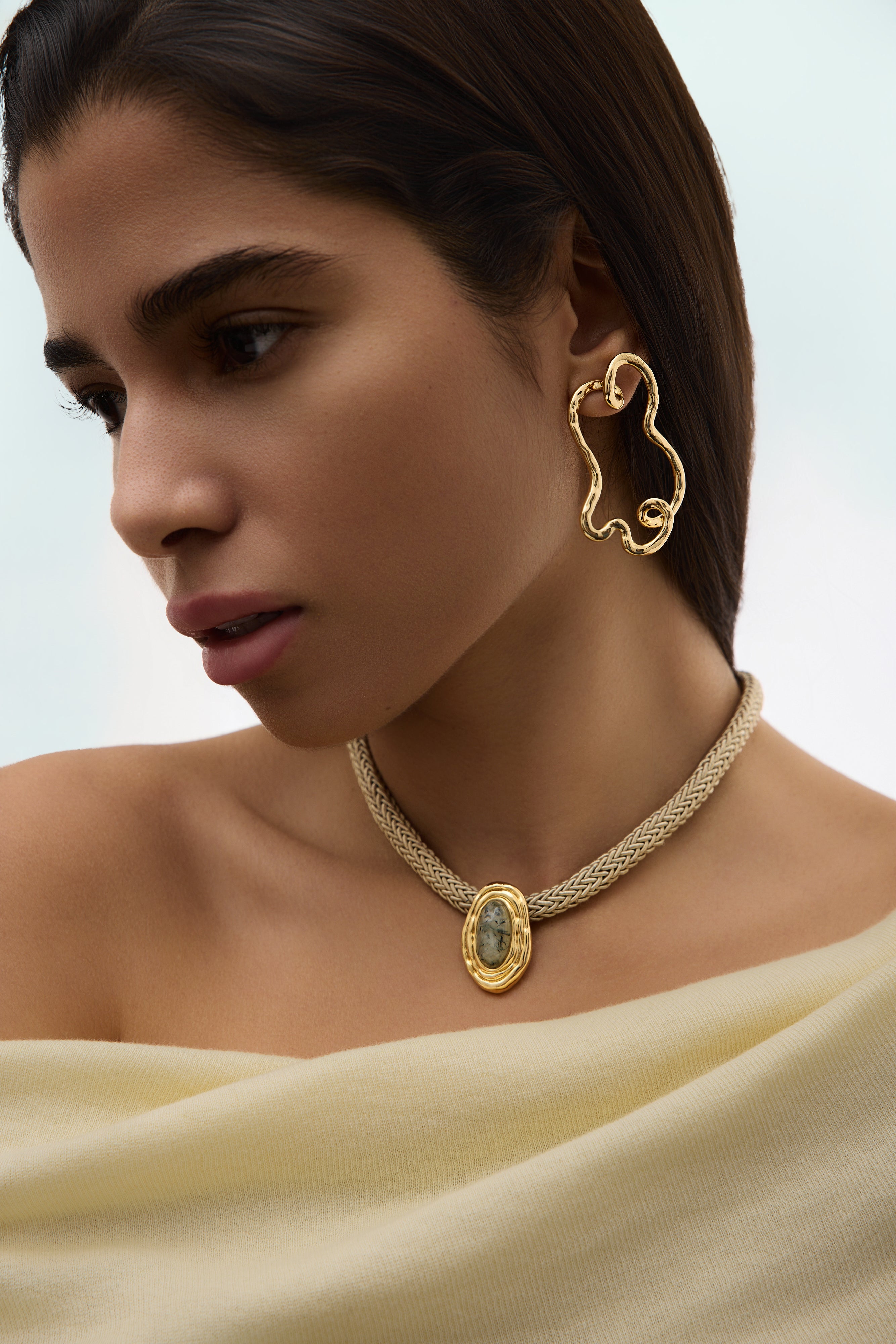 Woman wearing gold earrings and necklace against a neutral background