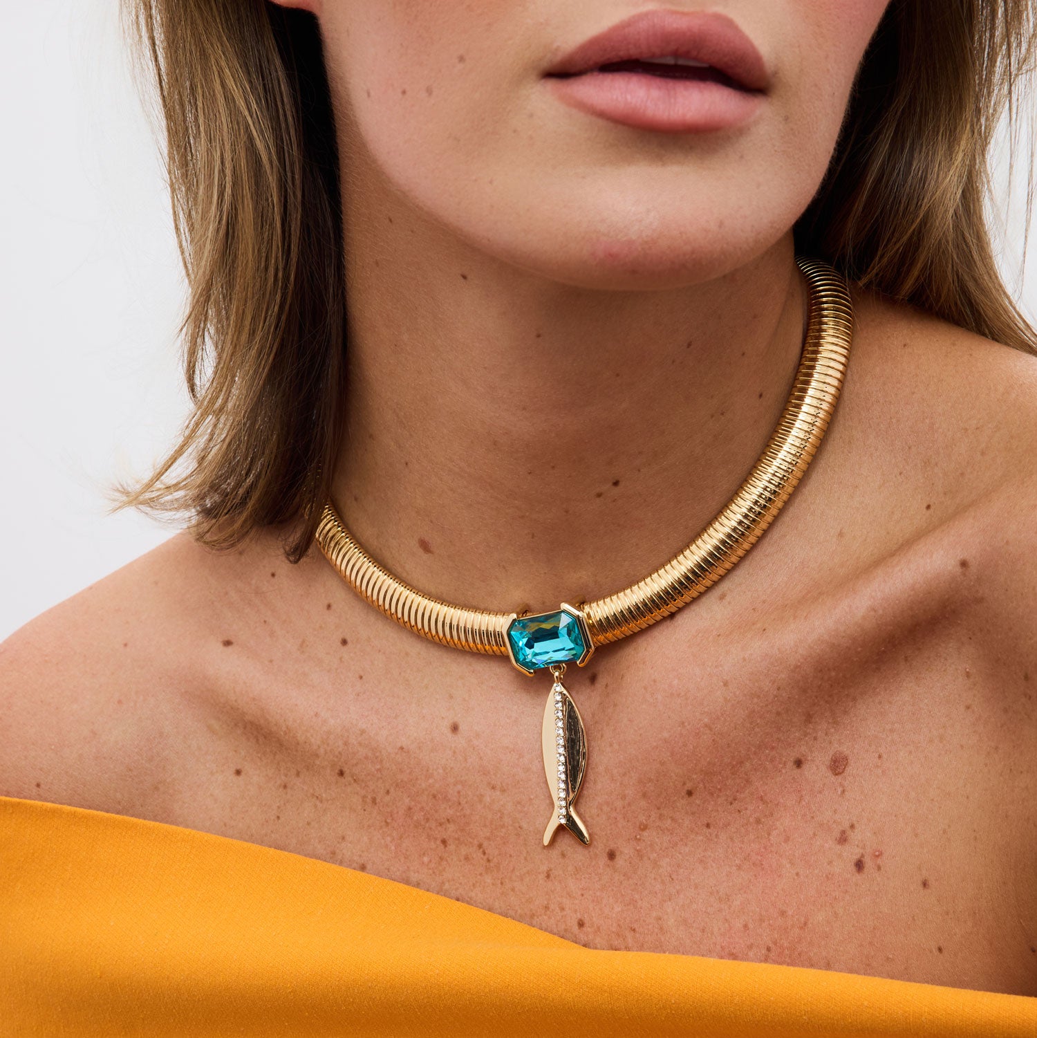 woman wearing a gold neckace with a gold fish and blue crystal wearing an orange shirt