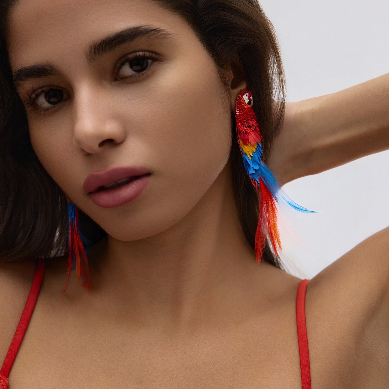 Woman wearing colorful parrot-shaped earrings with a neutral background