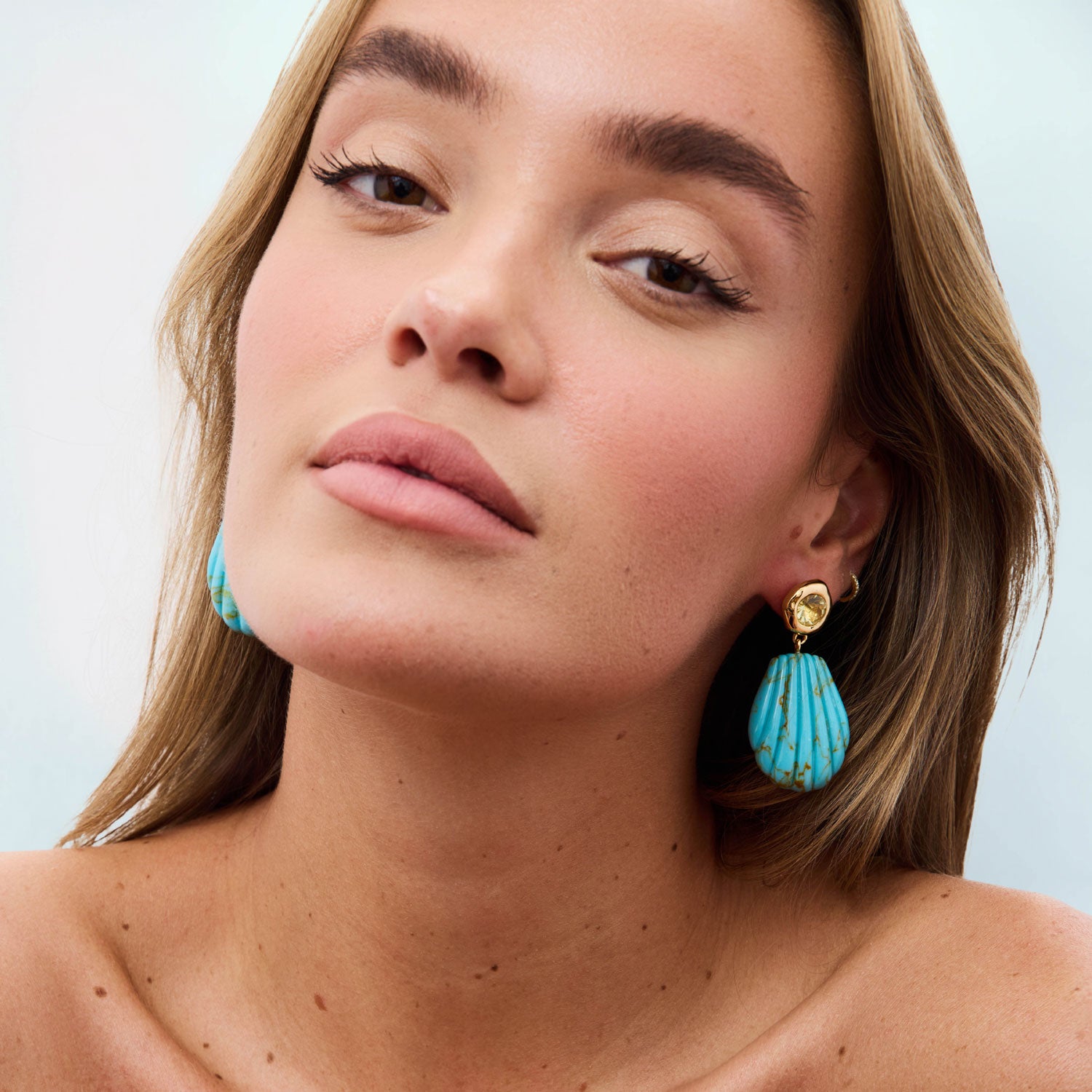 Woman wearing turquoise earrings with a plain background
