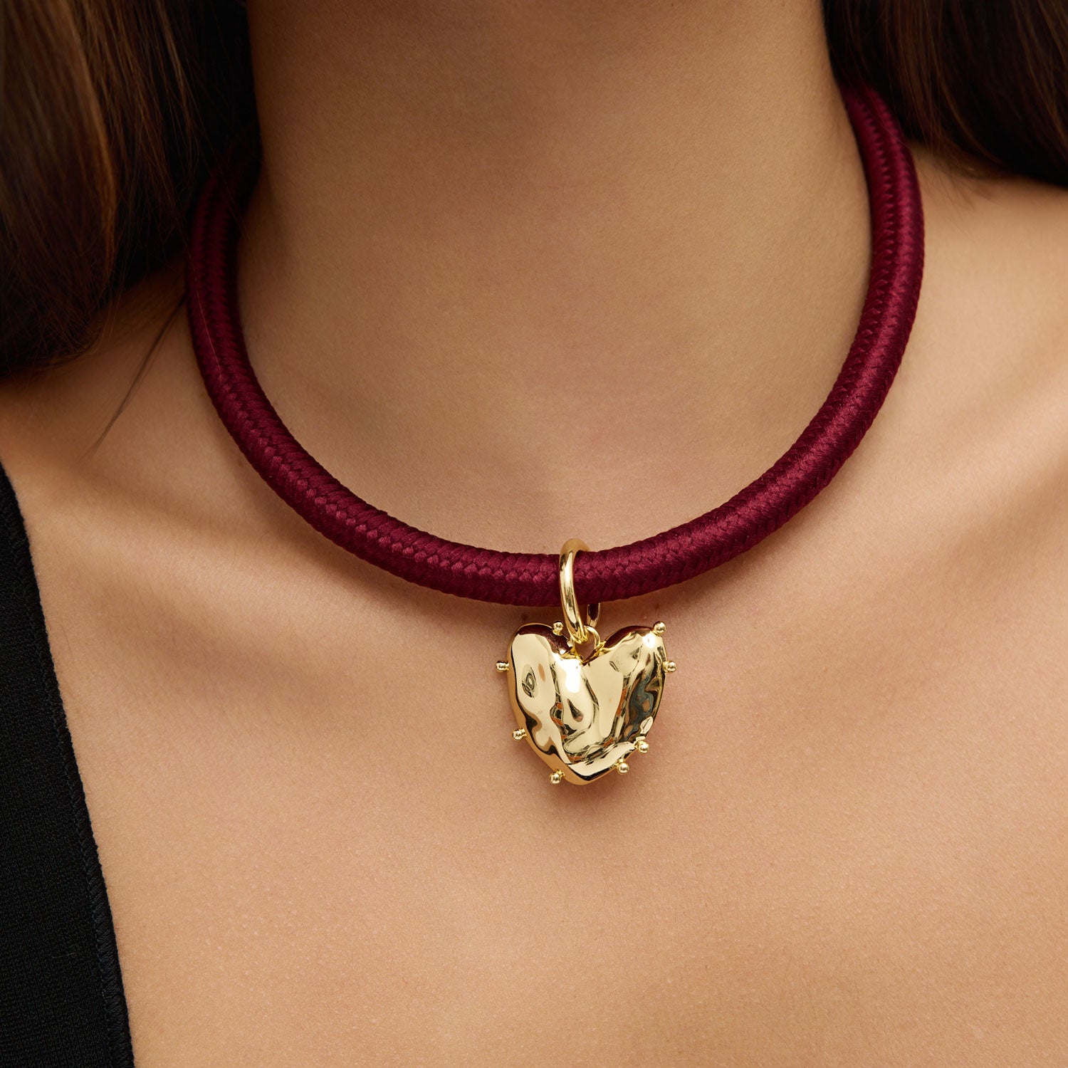 Gold heart-shaped pendant on a maroon cord necklace worn by a person.