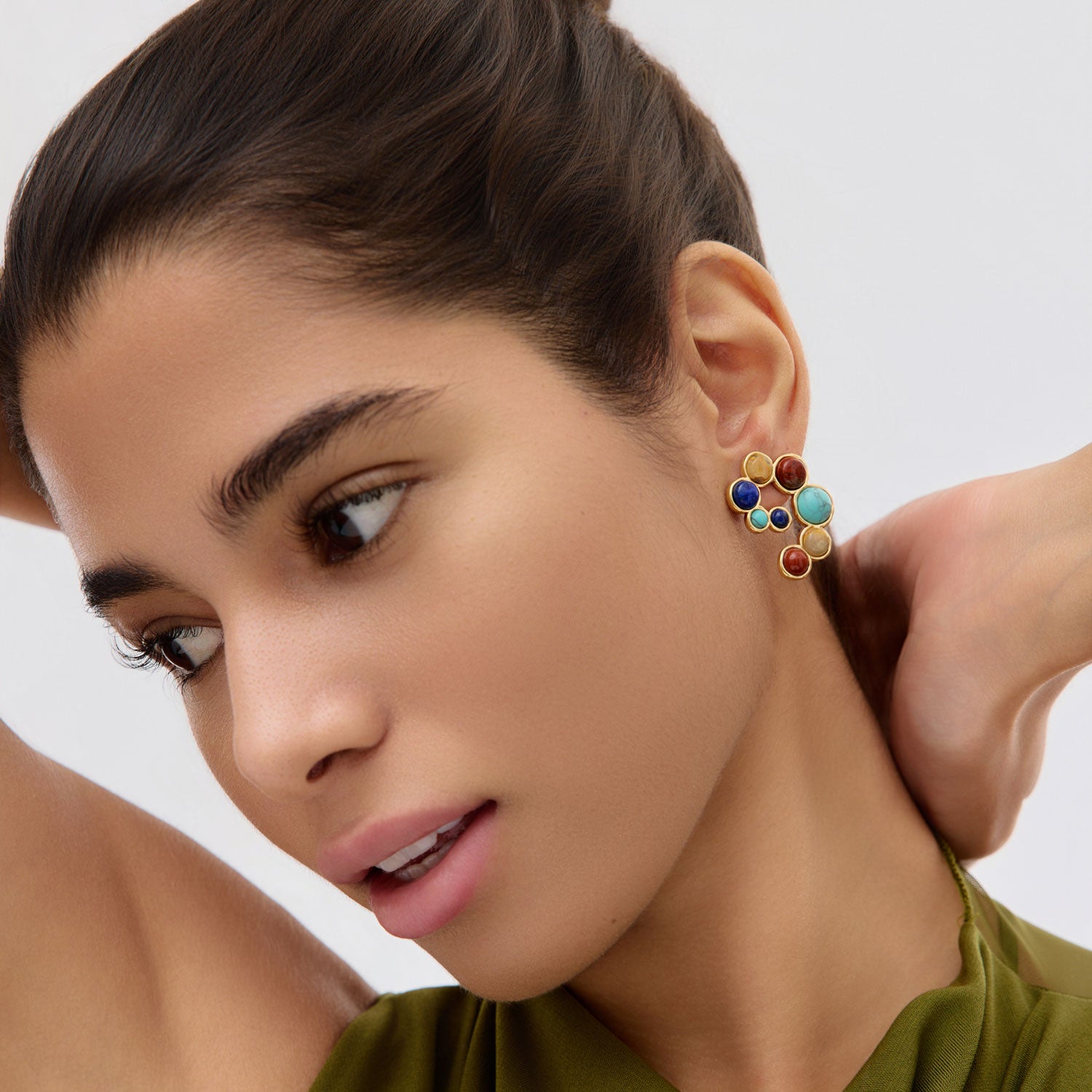 Close-up of a woman wearing colorful stone and gold earrings with a neutral background
