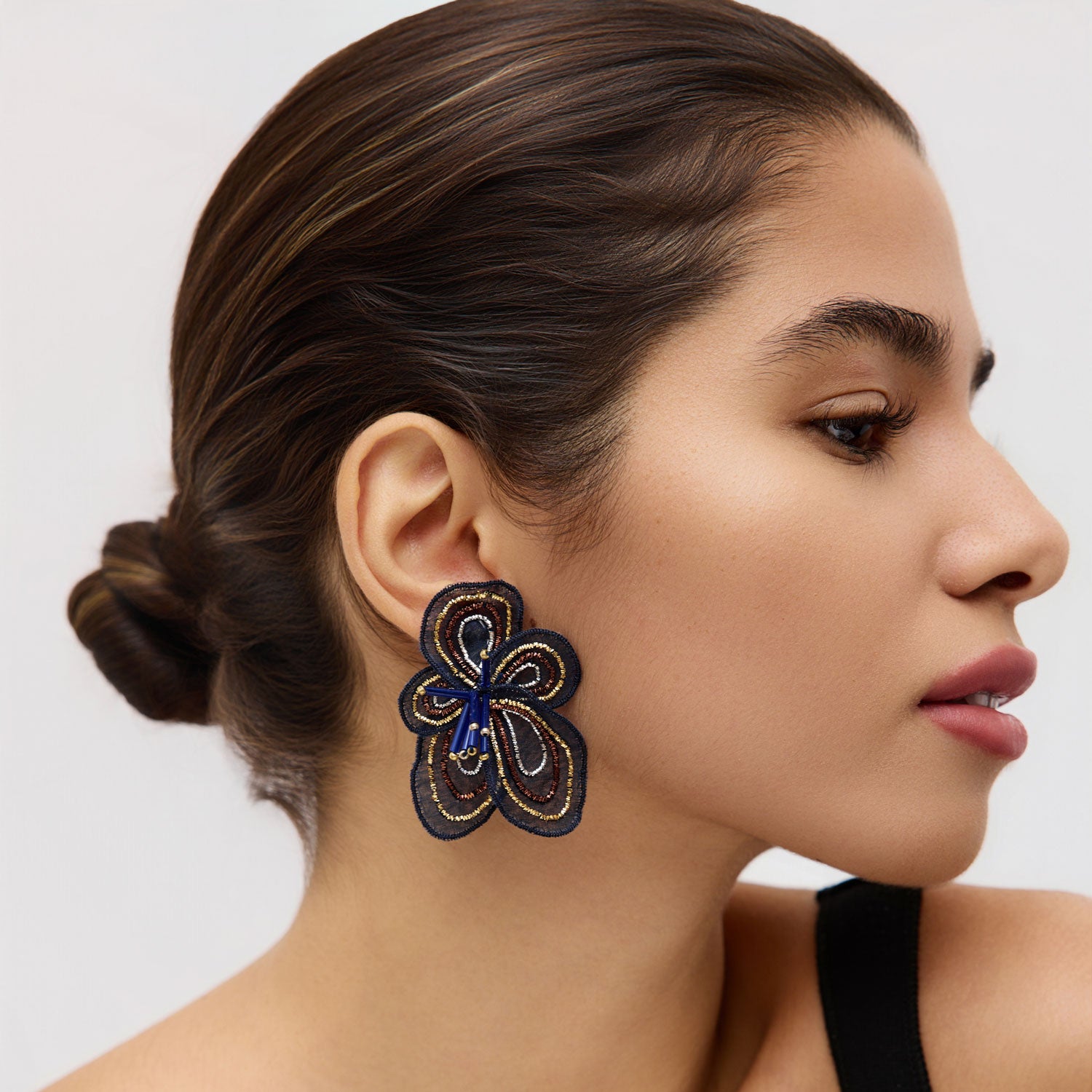 Woman wearing a navy floral earring with a neutral background