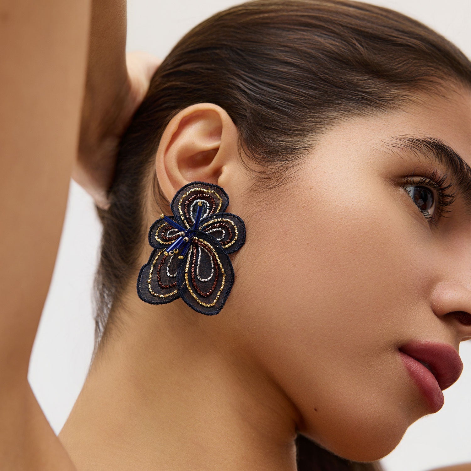 Woman wearing a navy floral earring with a neutral background