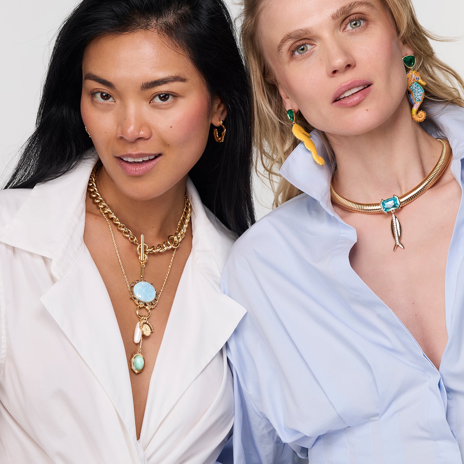 Two women wearing gold necklaces with various pendants on a white background