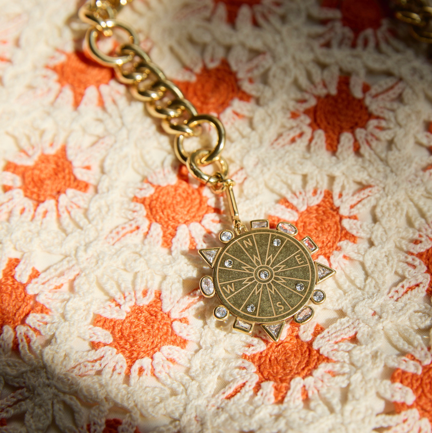 Gold pendant with crystals and compass etching against orange and white crochet background