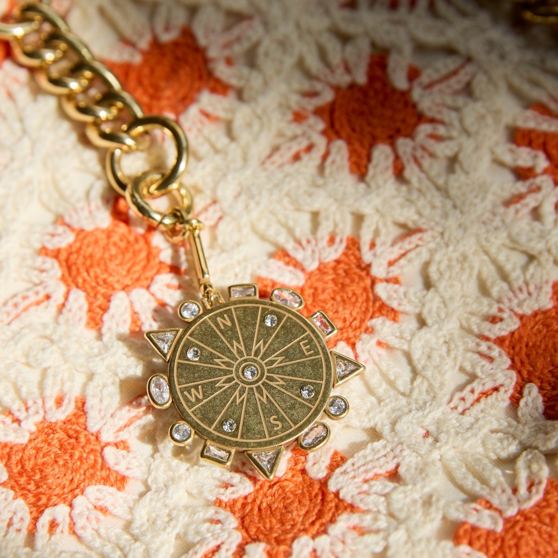 Gold compass charm with rhinestones on a textured orange and white surface