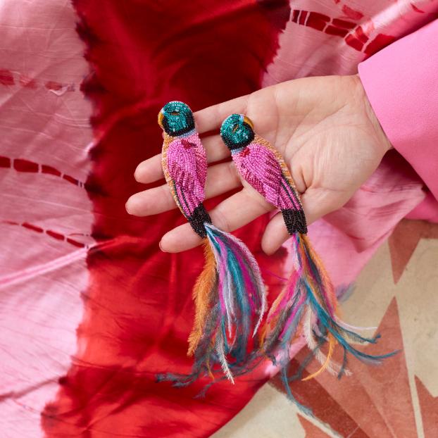 Hand holding two colorful embroidered bird keychains against a red fabric background