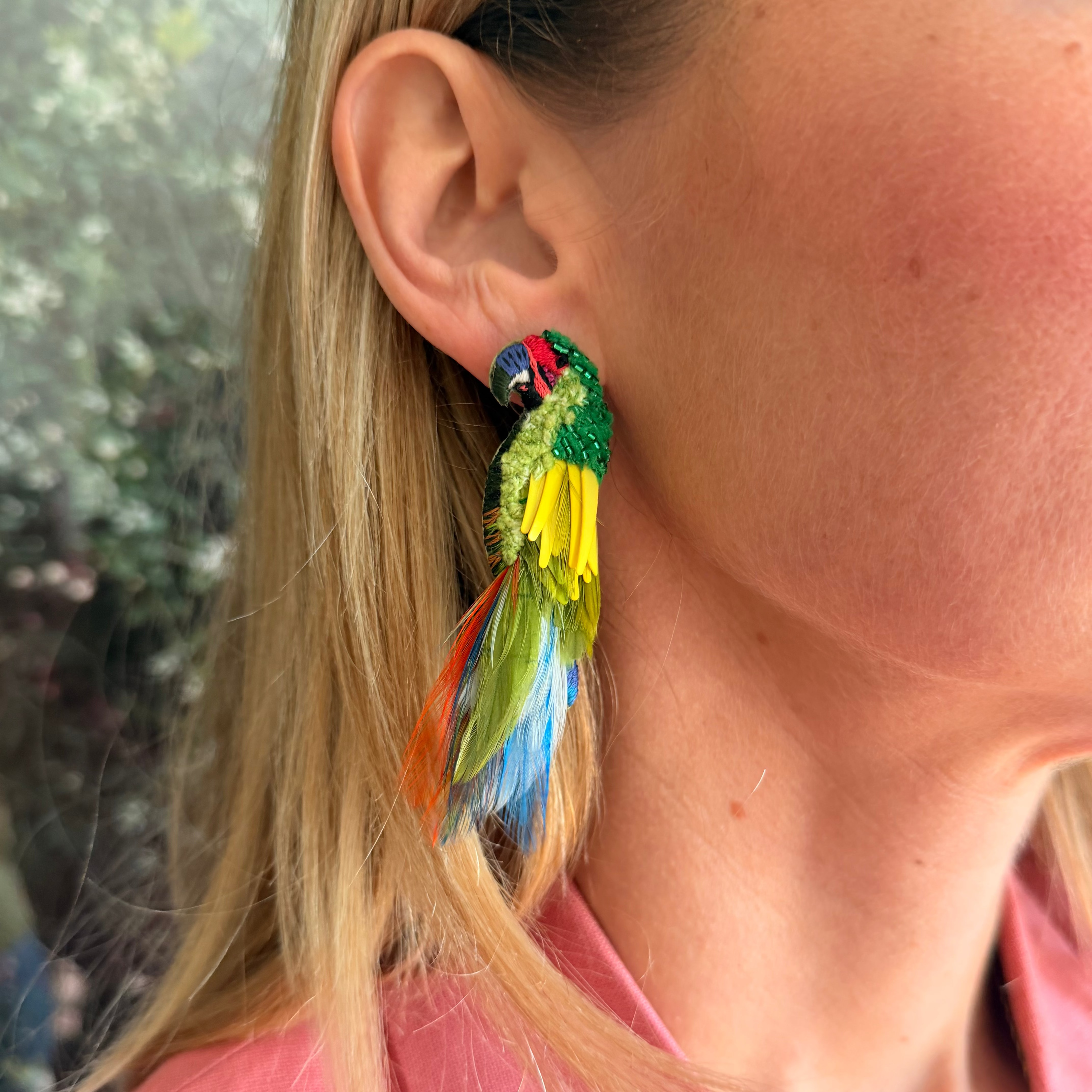 Close-up of a colorful feathered earring worn by a person with a blurred background