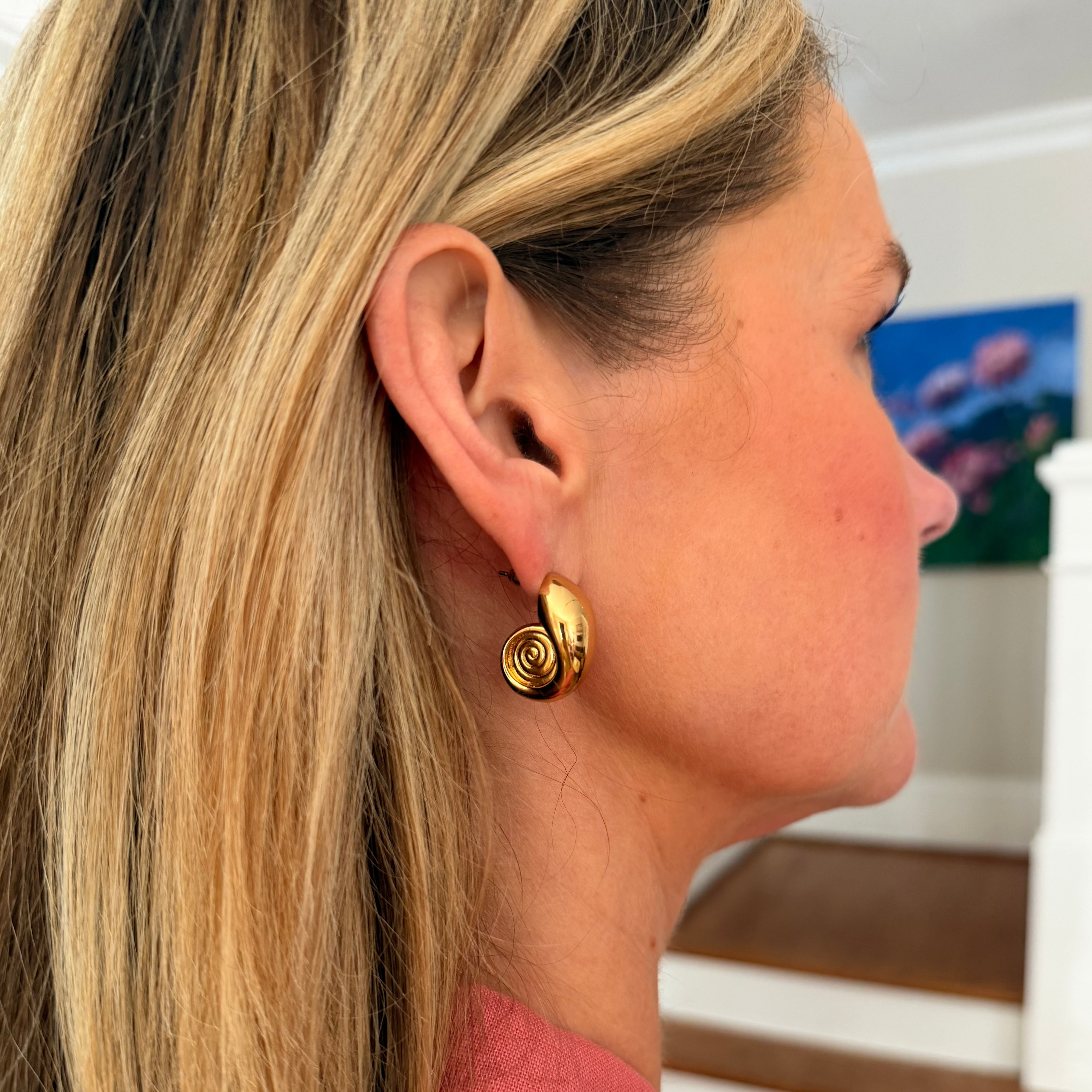 Close-up of a woman wearing gold spiral earrings with a blurred indoor background.