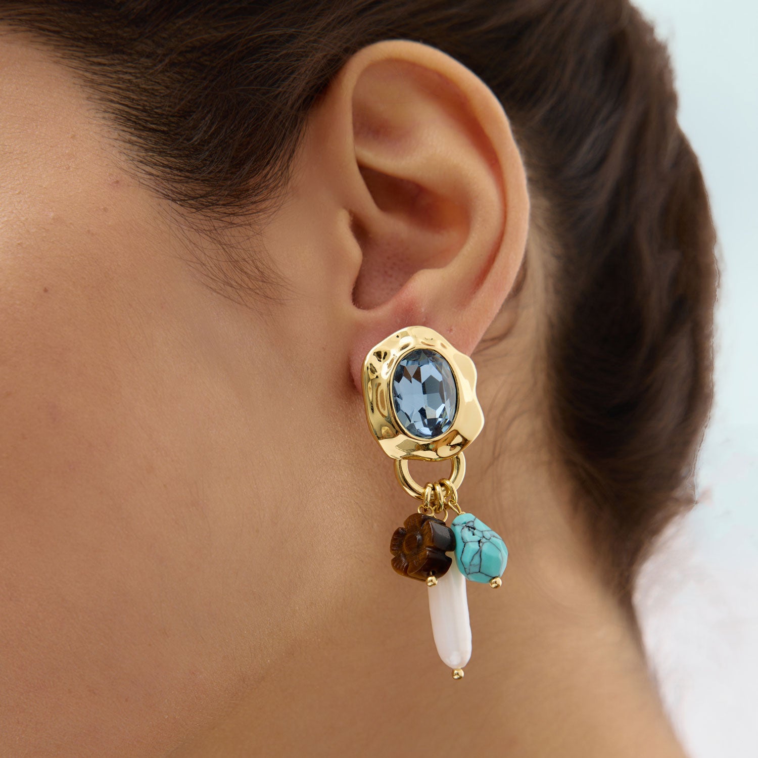 Close-up of an ear wearing a gold earring with colored gemstones.