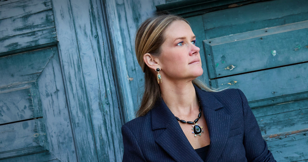 Model wearing statement earrings and necklace on a blue background