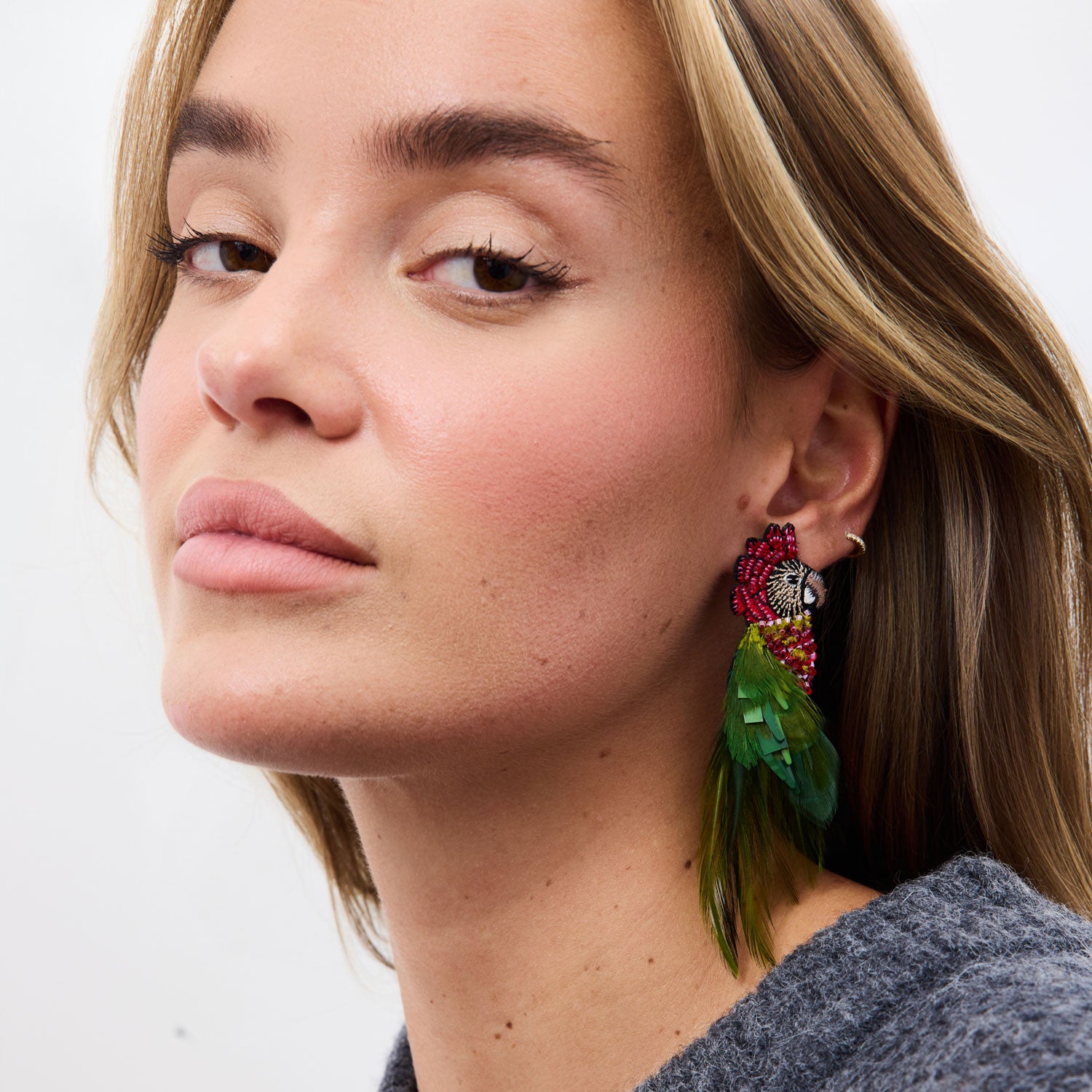 Close-up of a woman wearing colorful bird feather earrings with a neutral background