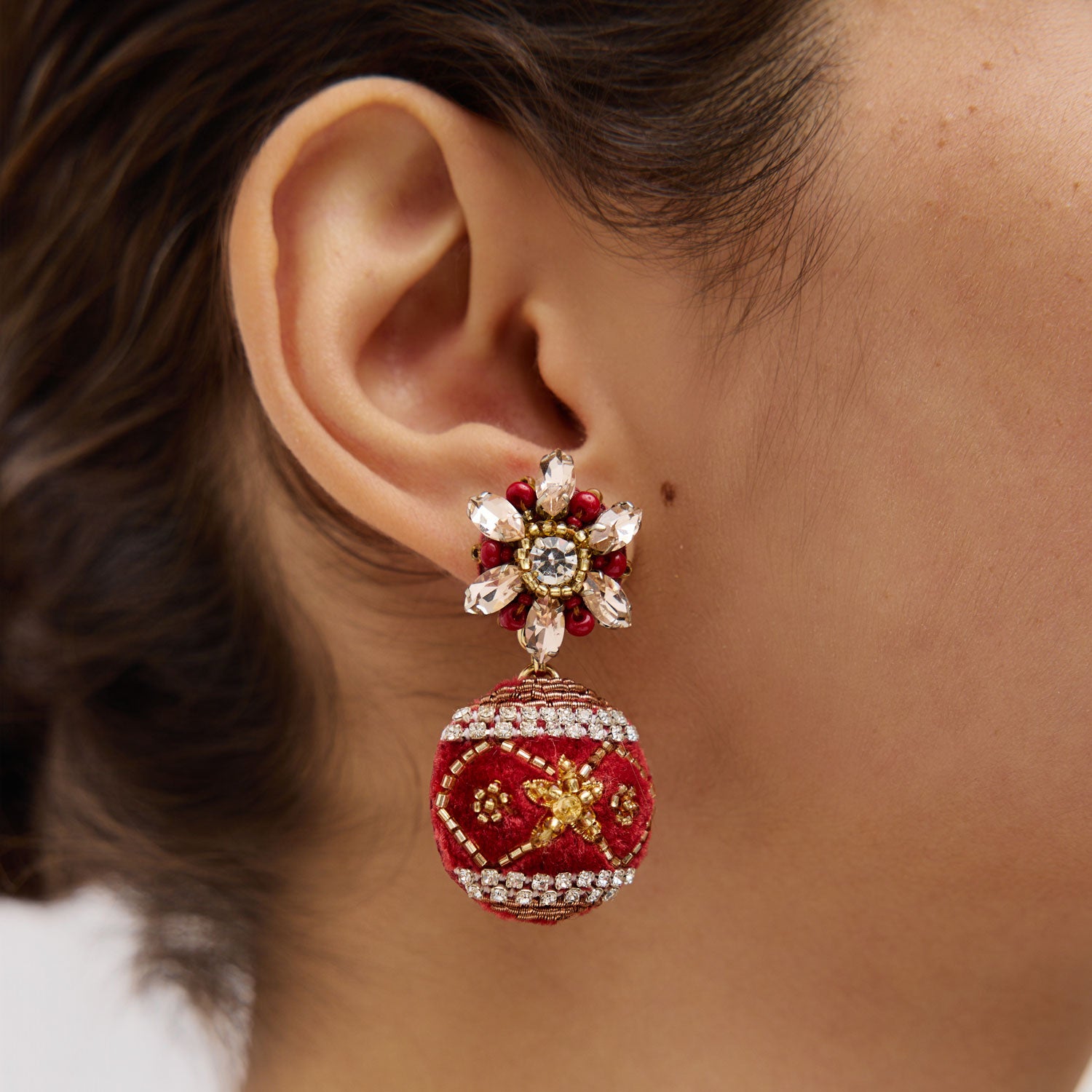 Close-up of an ear wearing a decorative red and gold ornament drop earring.
