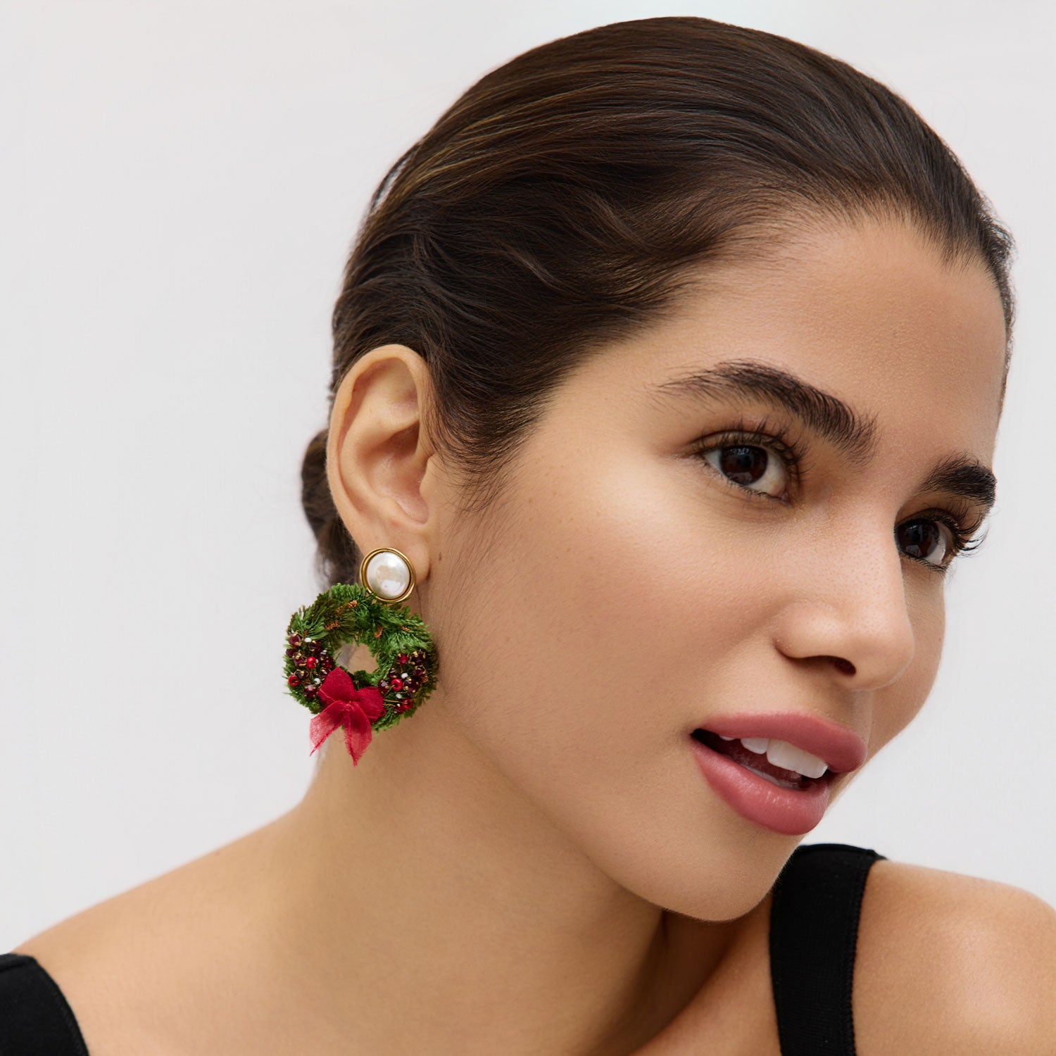 Woman wearing a festive earring with a green wreath and red bow on a plain background