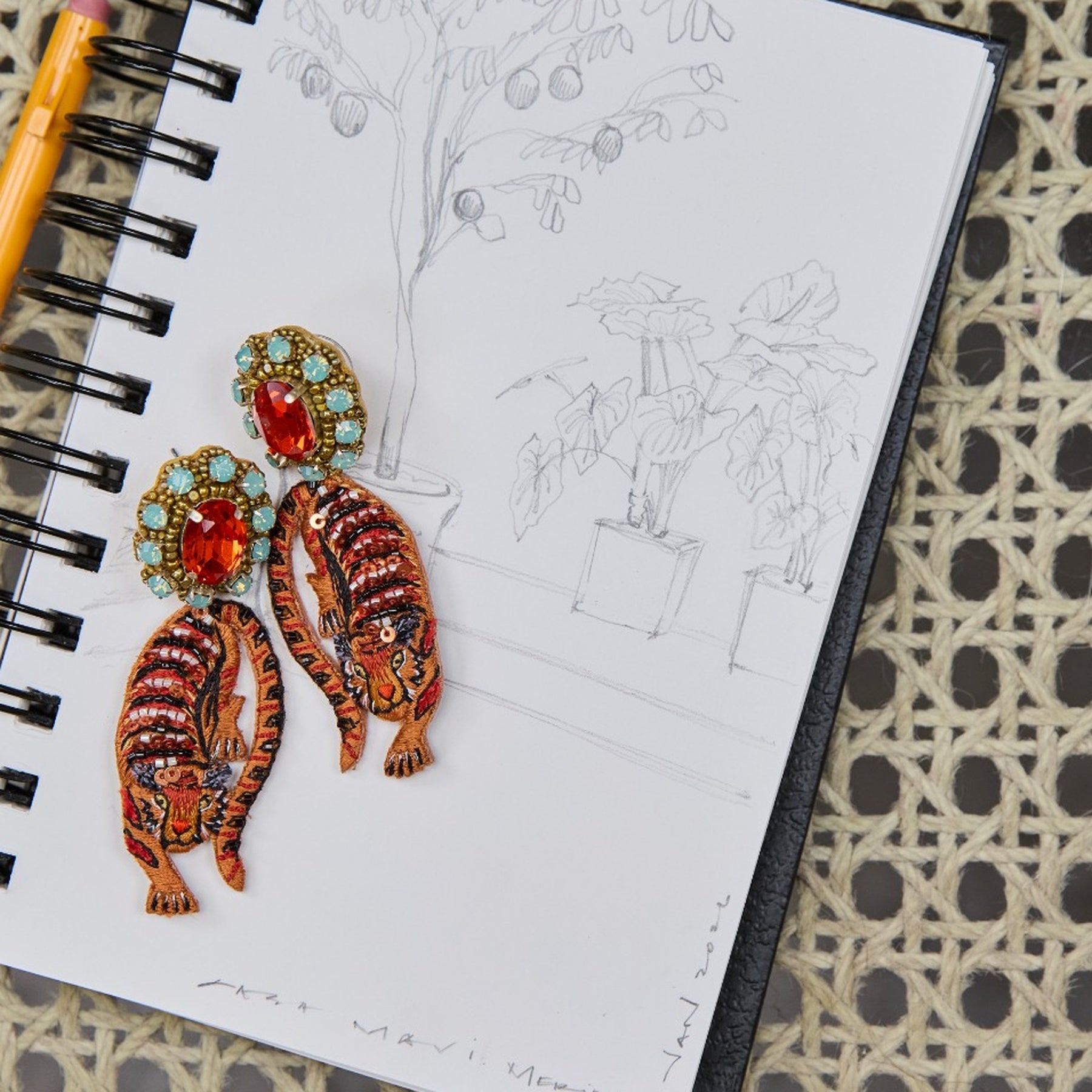 Colorful tiger-shaped earrings on a notebook with sketches