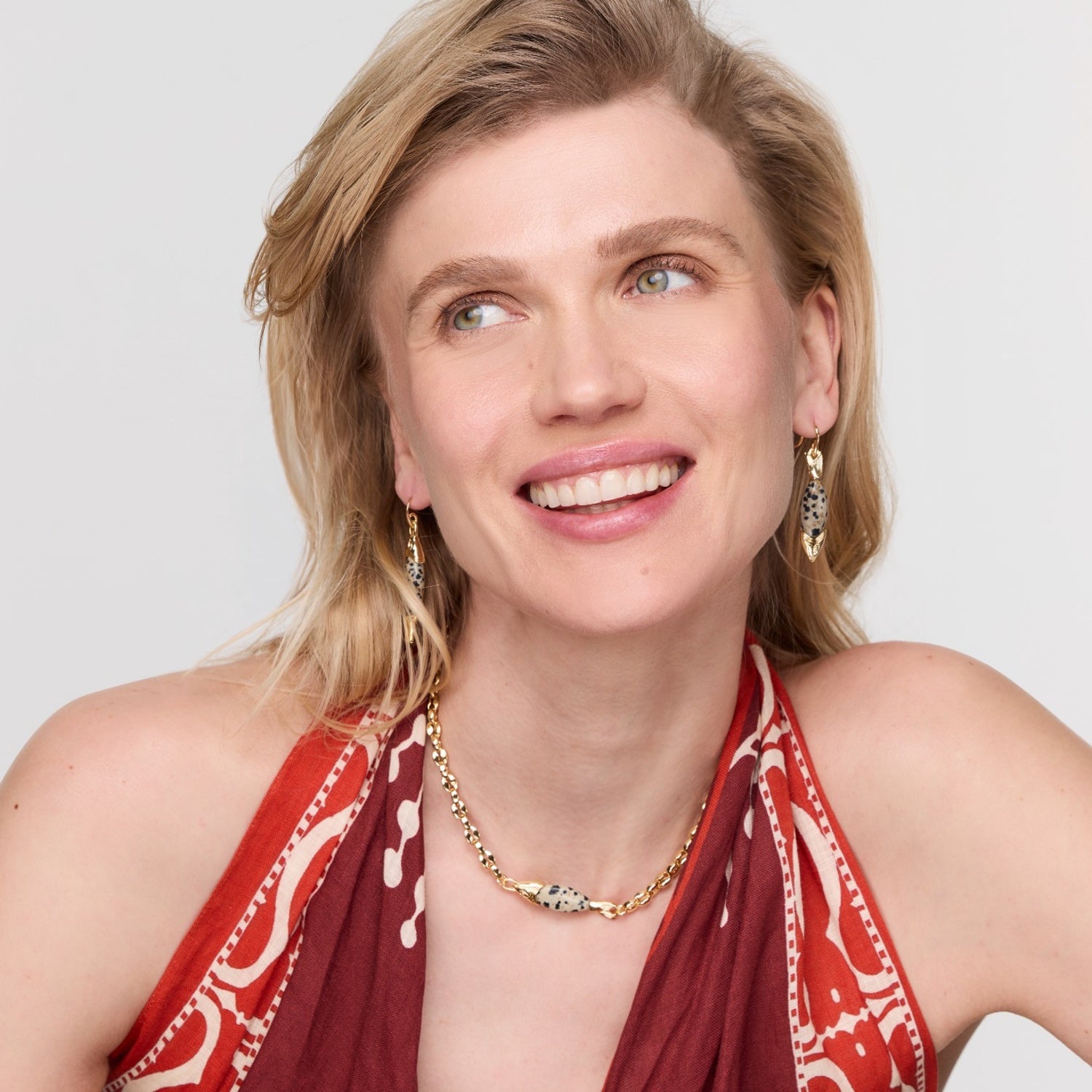 Woman wearing a red patterned top and gold jewelry against a white background