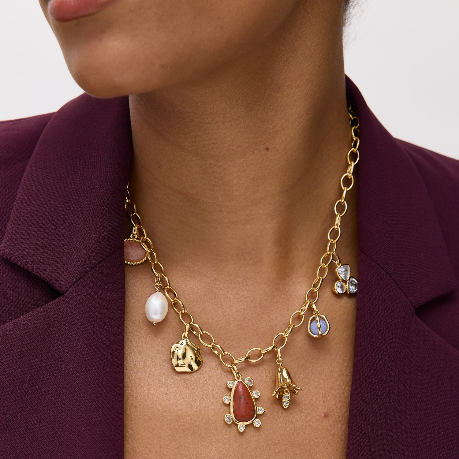 Gold necklace with various charms worn by a person against a plain background